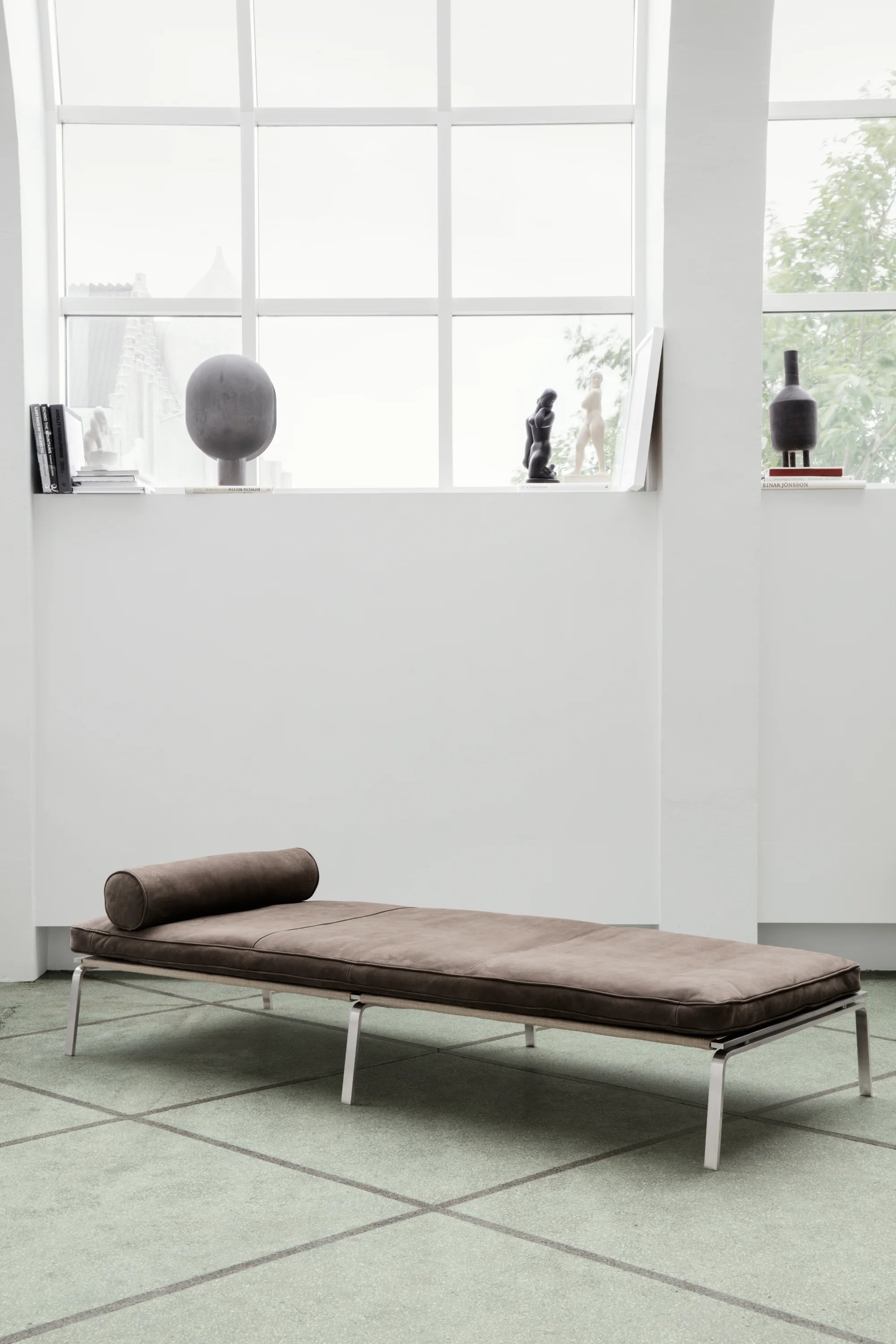 Modern brown daybed with metal frame in a room with large windows.