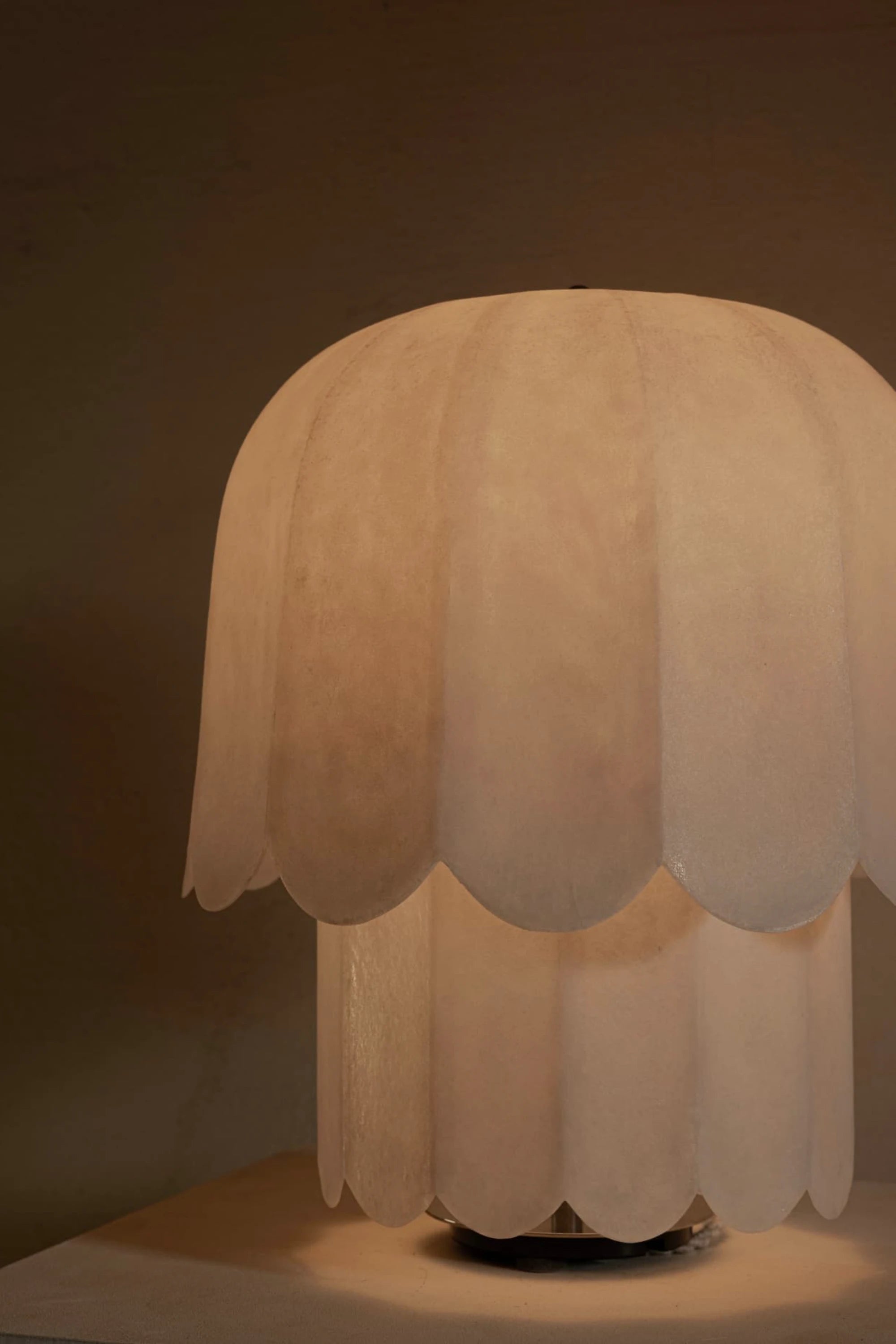 White scalloped-edge kilzi feather table lamp on a mood lit background