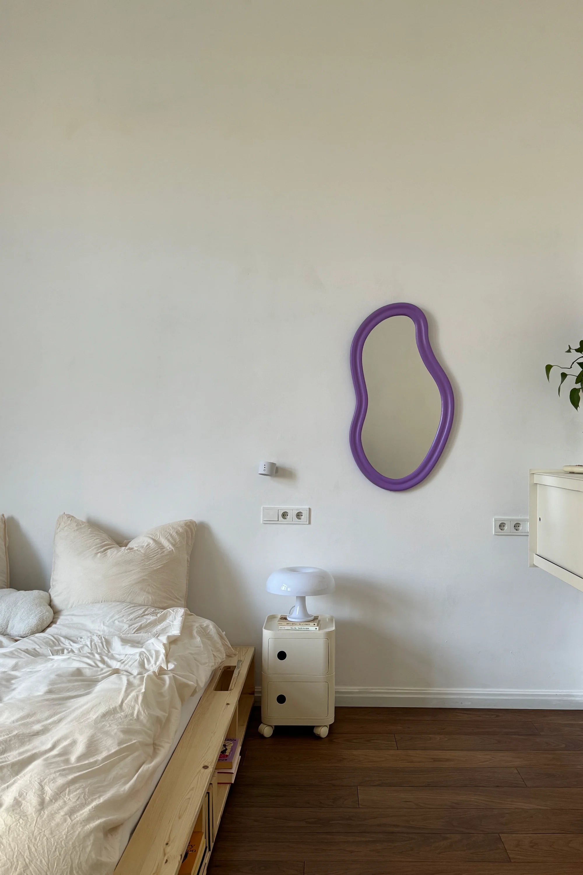 Bedroom with a purple mirror on the wall, a nightstand with a lamp, and a bed.