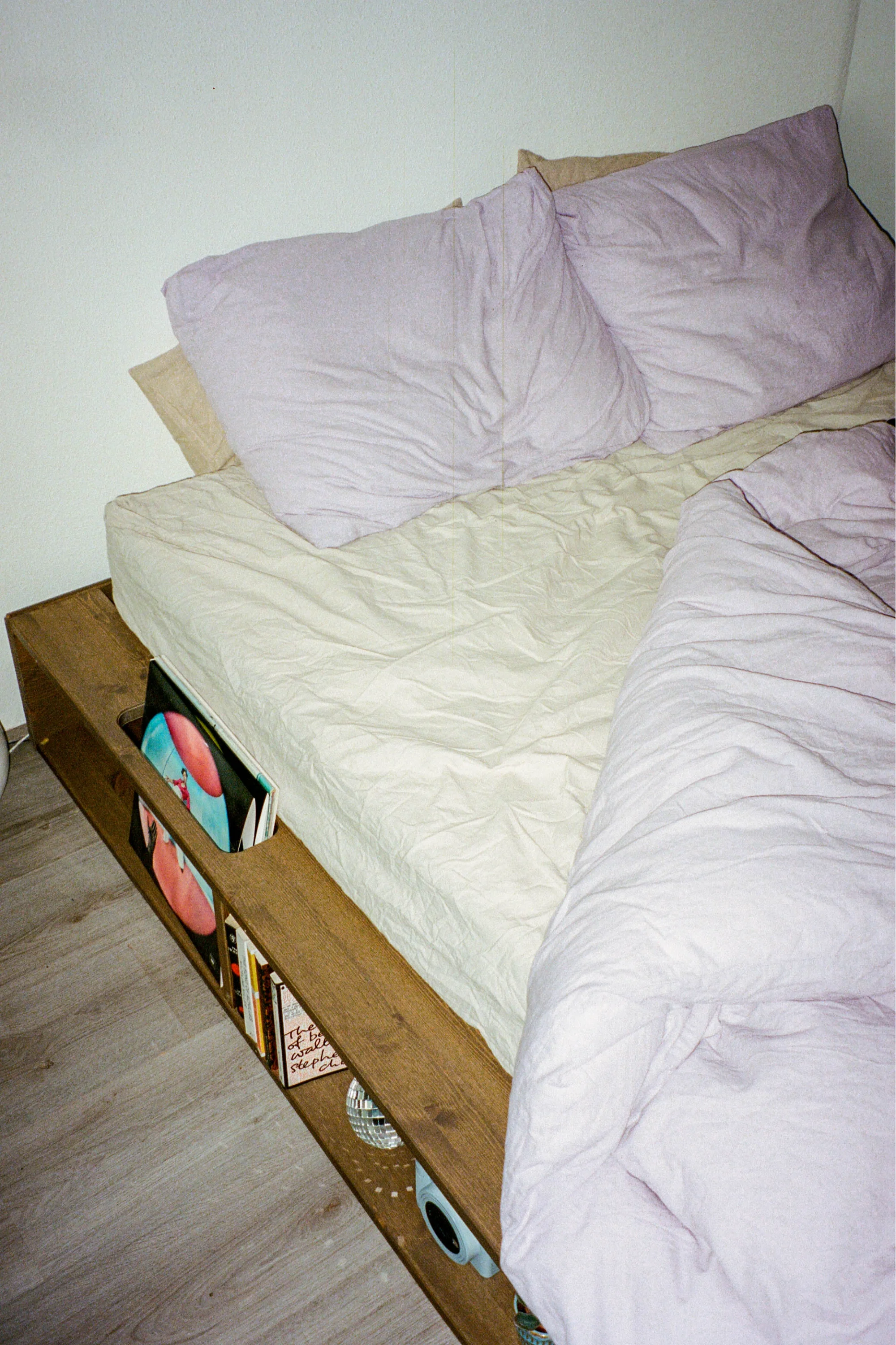 Bed with white bedding and purple pillows against a plain wall.