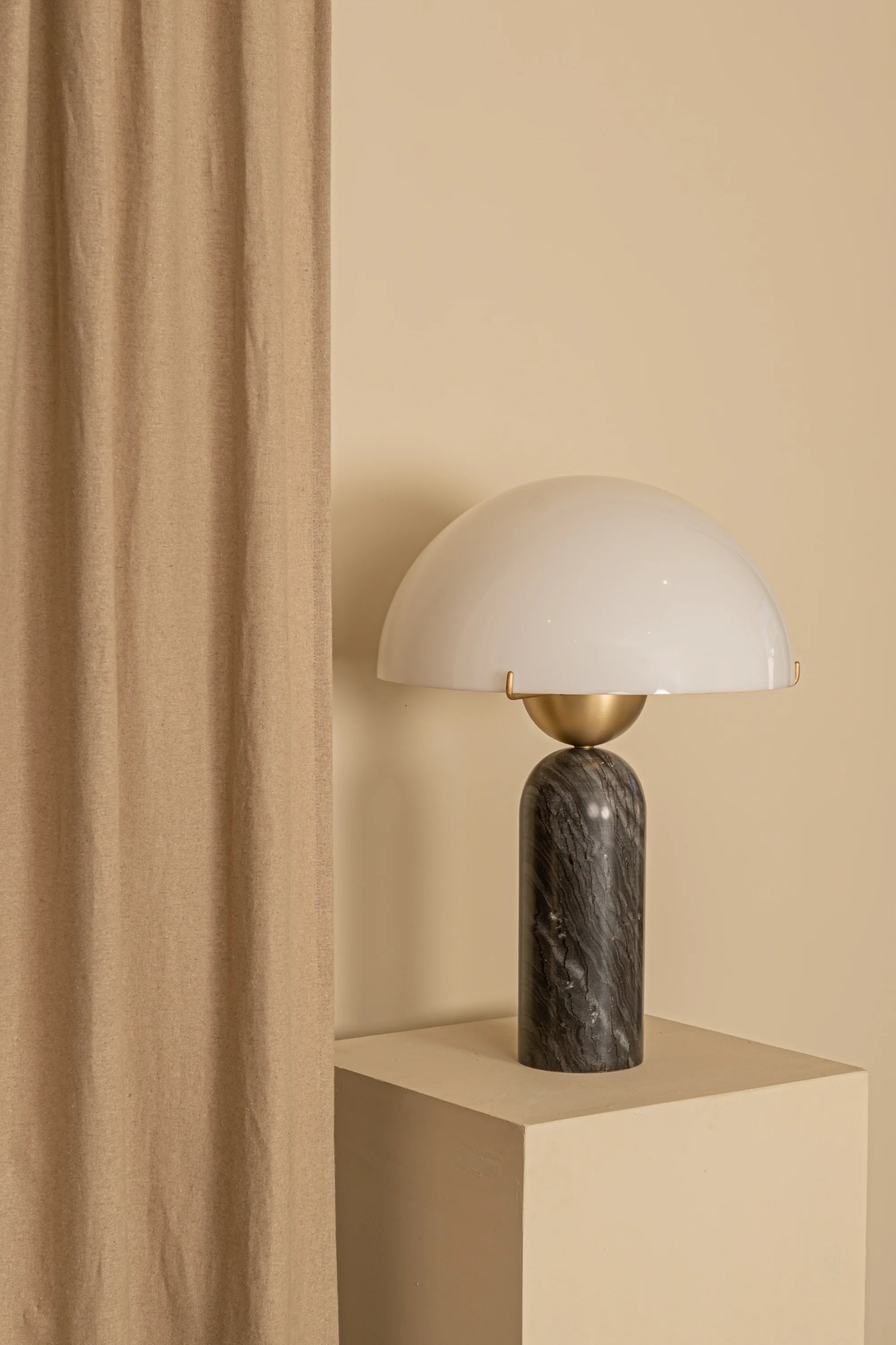 Table lamp with marble base and white shade on a beige pedestal against a beige wall.