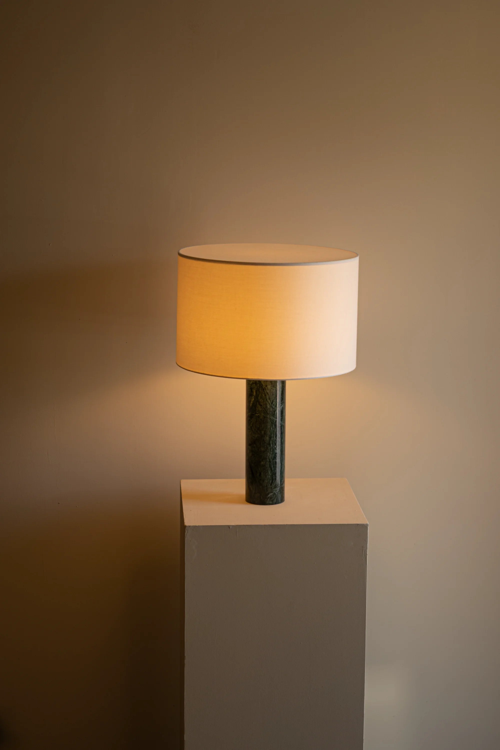 Table lamp with a beige shade on a gray pedestal against a brown background