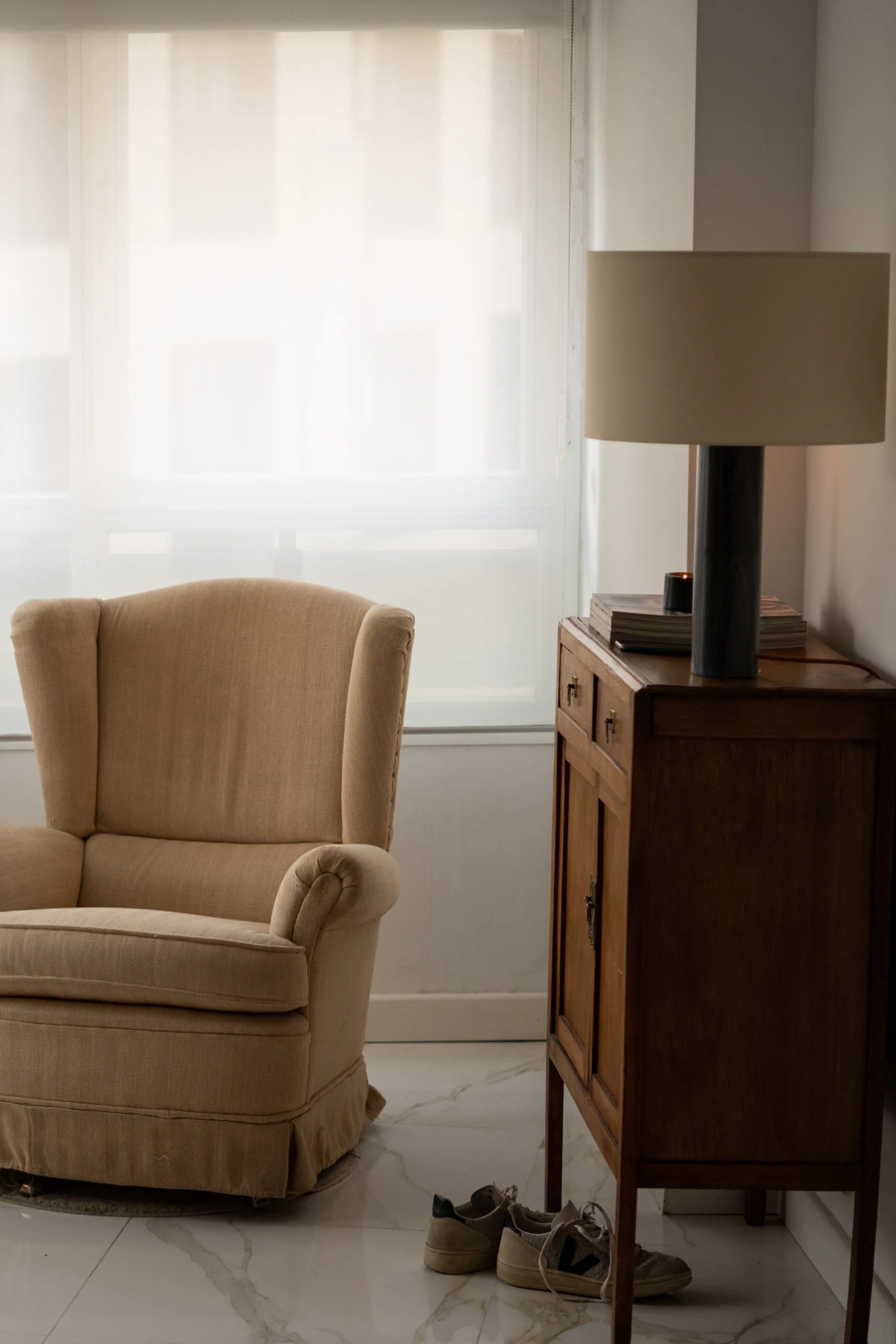 Beige armchair next to a wooden side table with a lamp in a room with striped wallpaper.