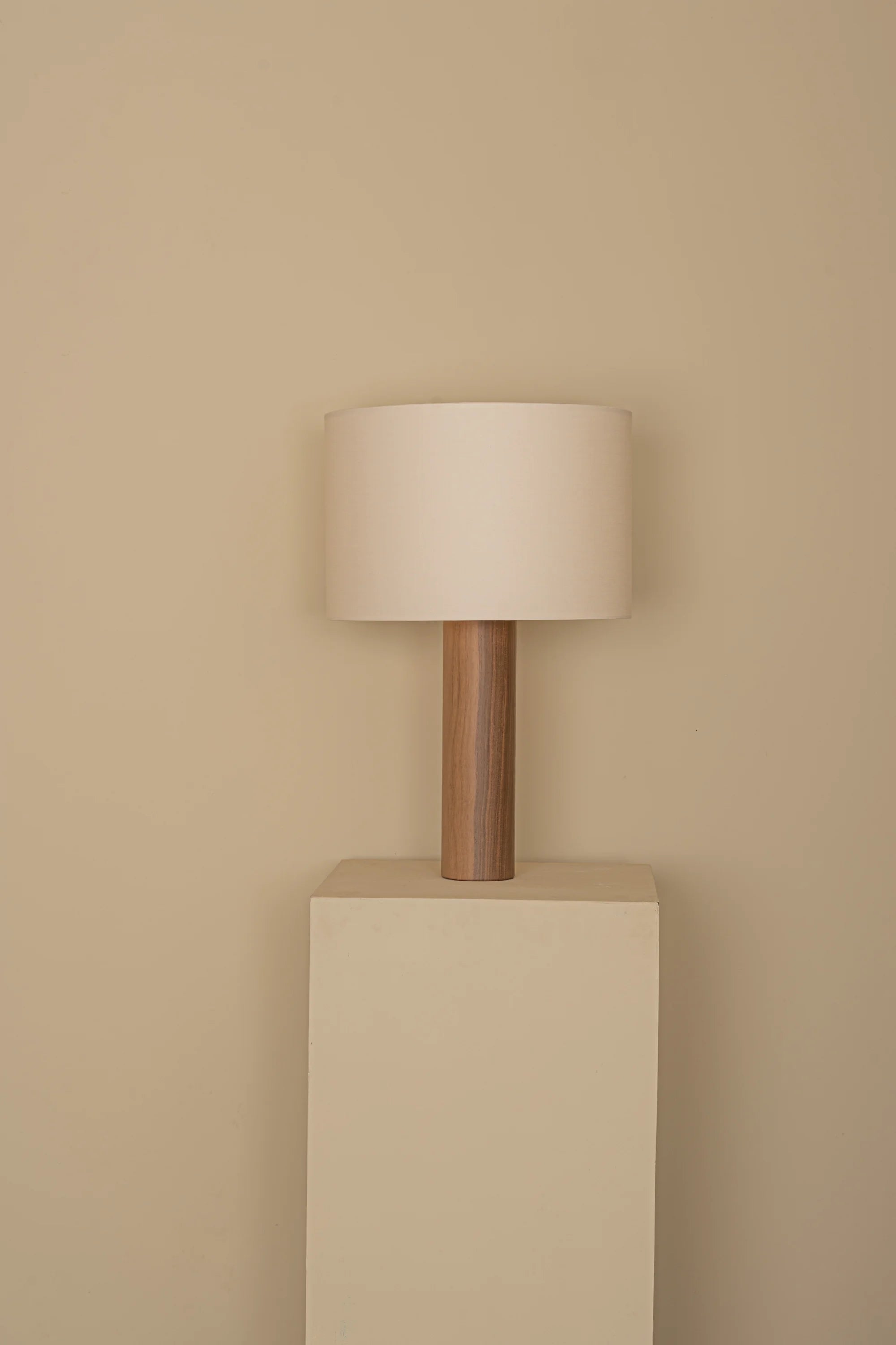Floor lamp with wooden base and beige shade against a beige wall