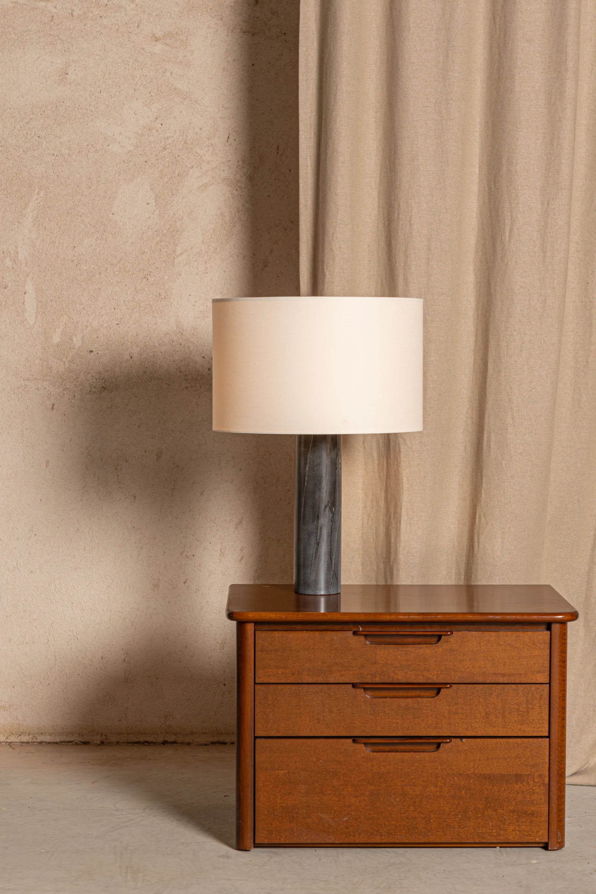 Wooden nightstand with a lamp against a beige curtain