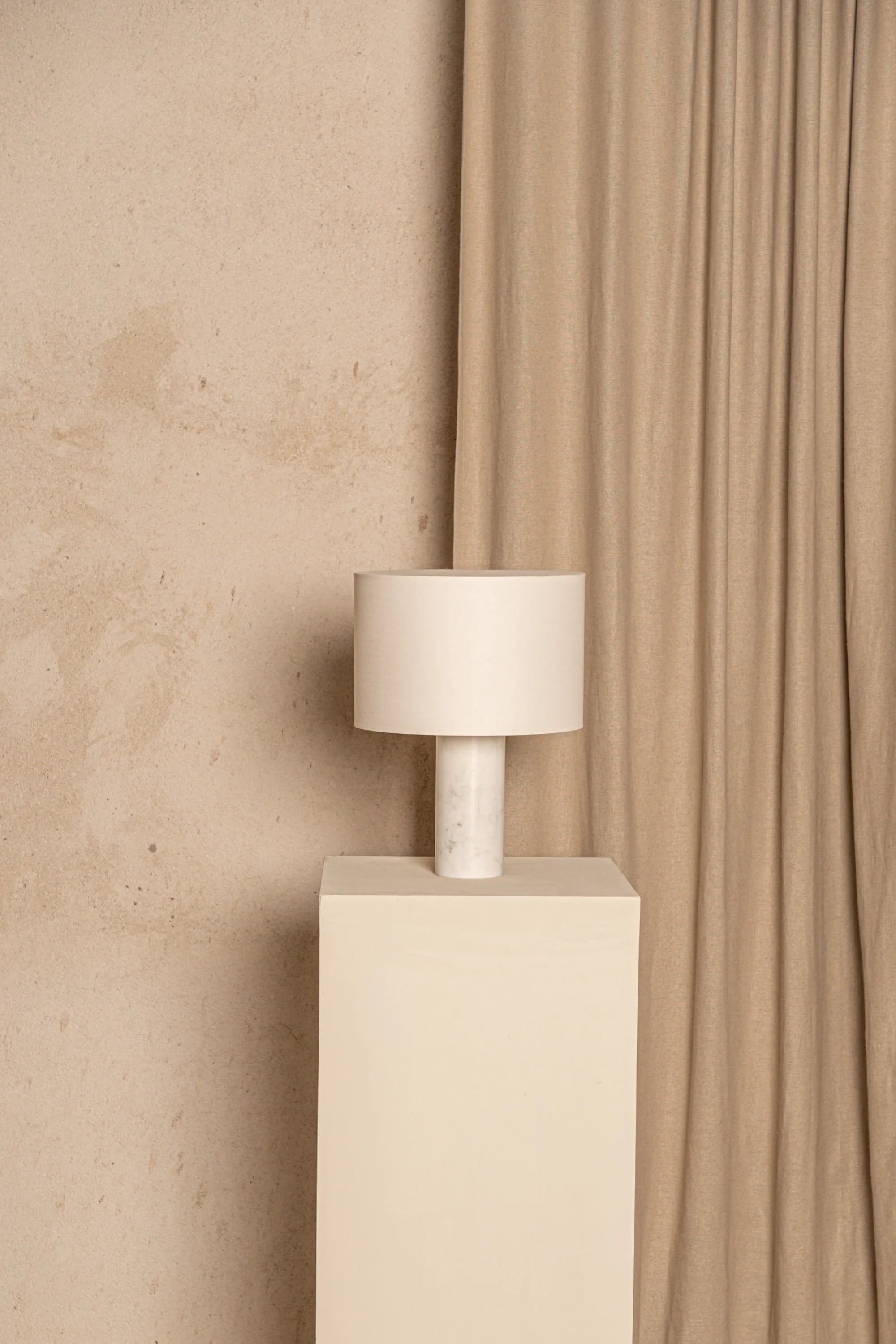 Beige lamp on a pedestal against a beige curtain and wall