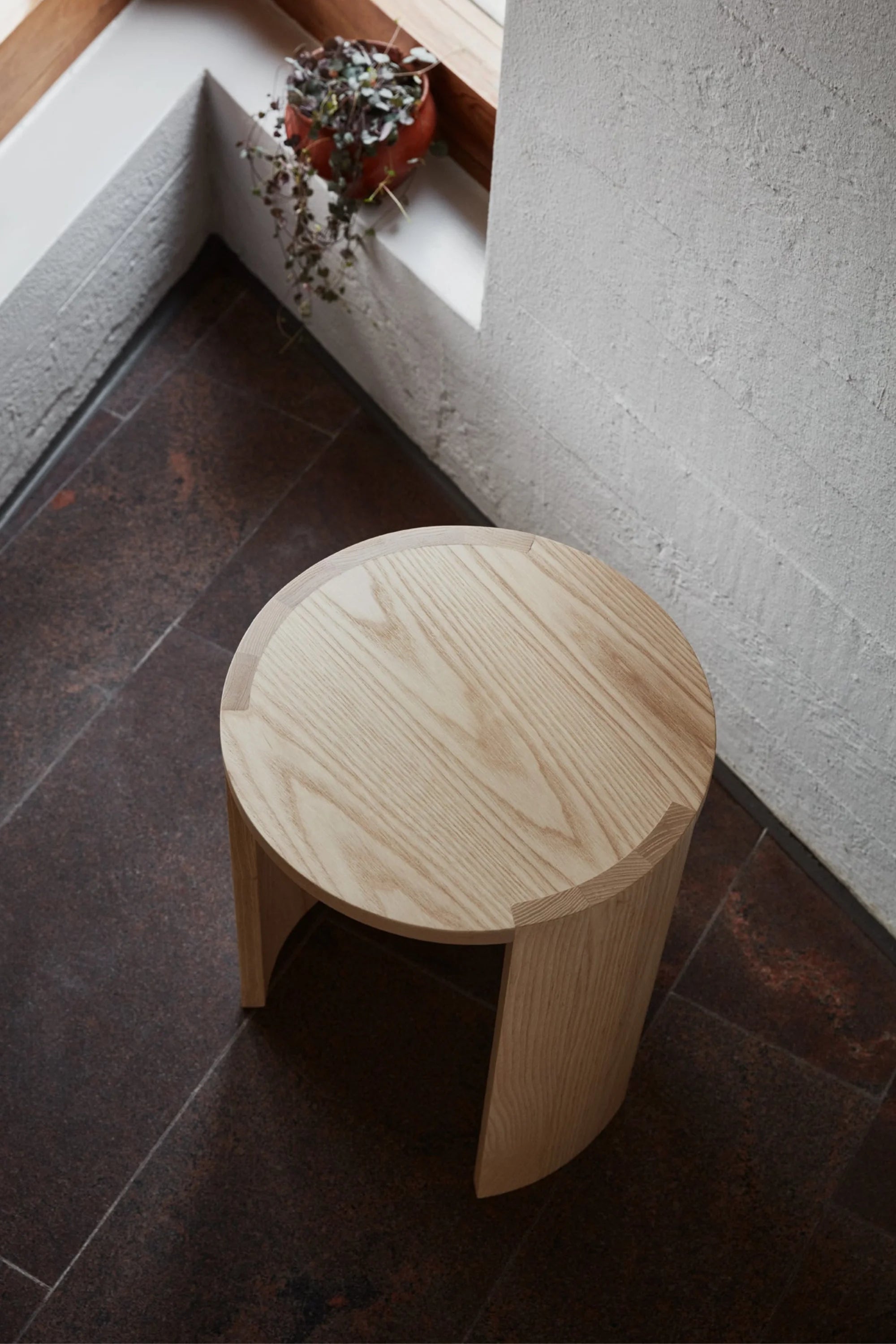 Wooden stool on a dark tiled floor with a light gray wall in the background.
