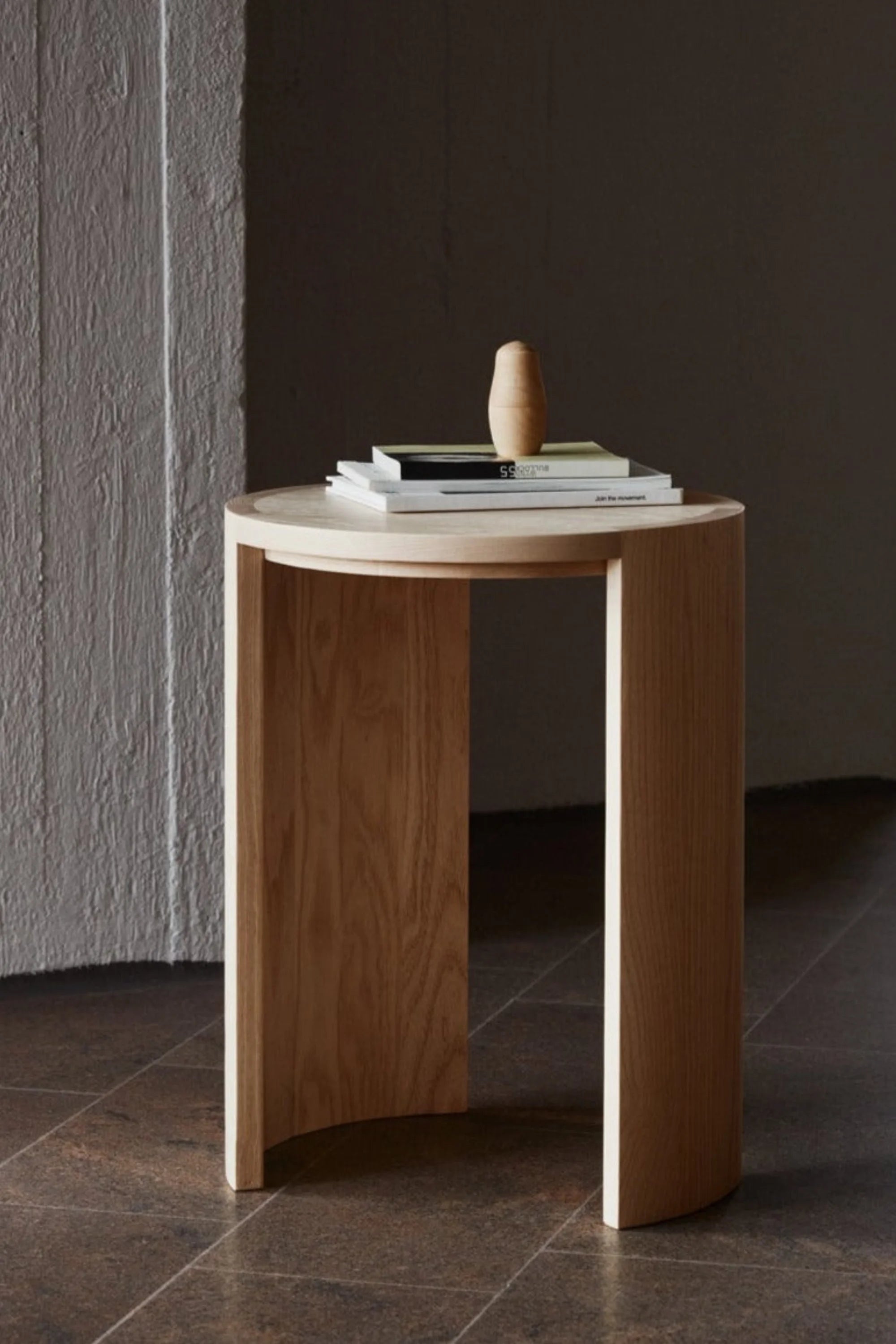 Wooden side table with a small sculpture on a dark floor against a gray wall