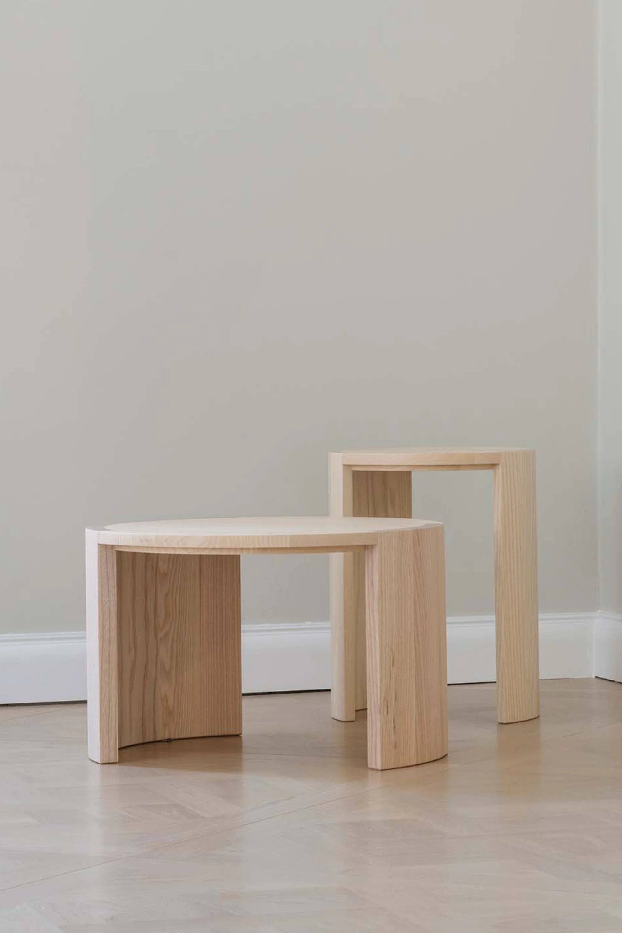 Two wooden stools on a light wood floor against a plain wall.