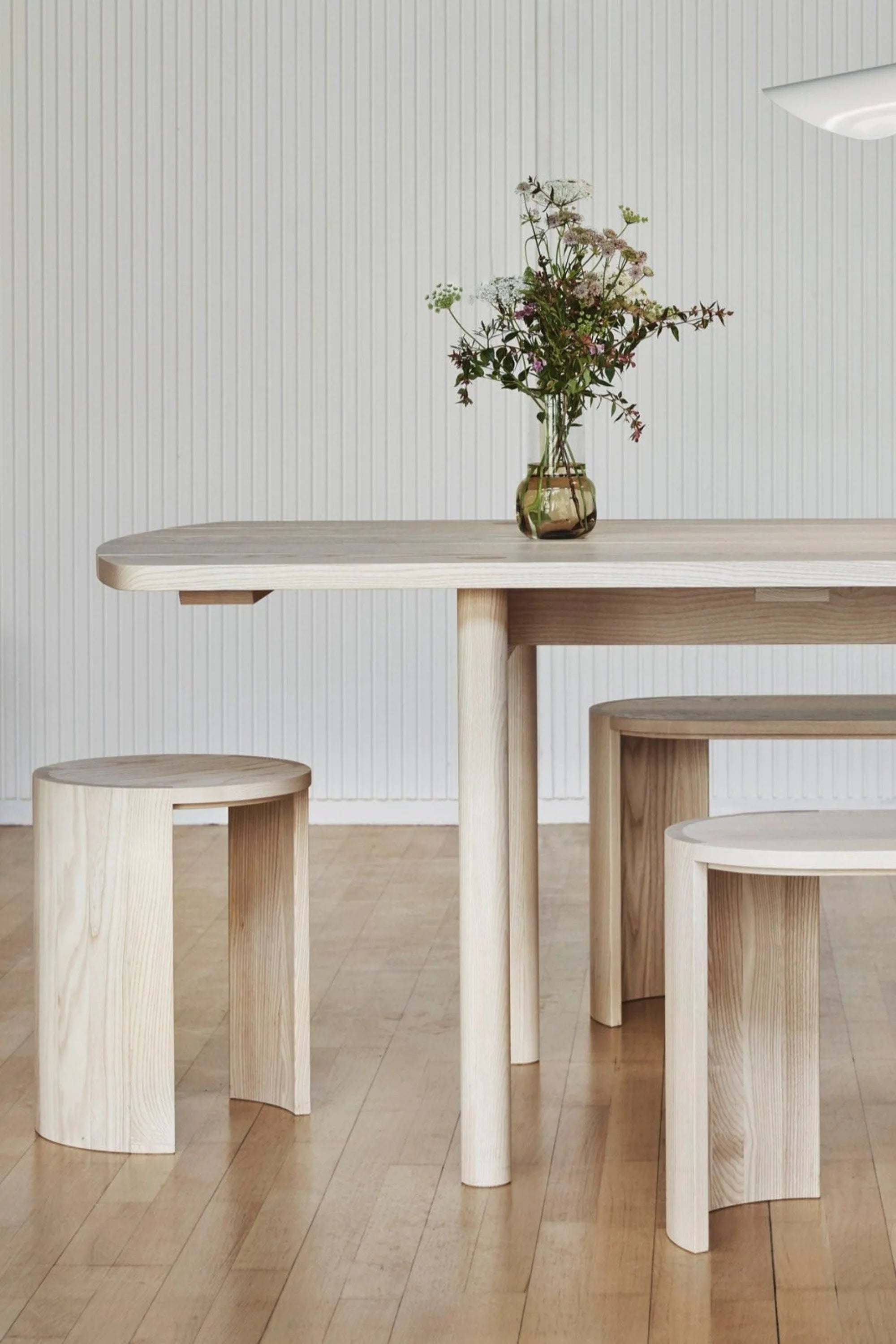 Dining area with a wooden table and stools against a light-colored wall.