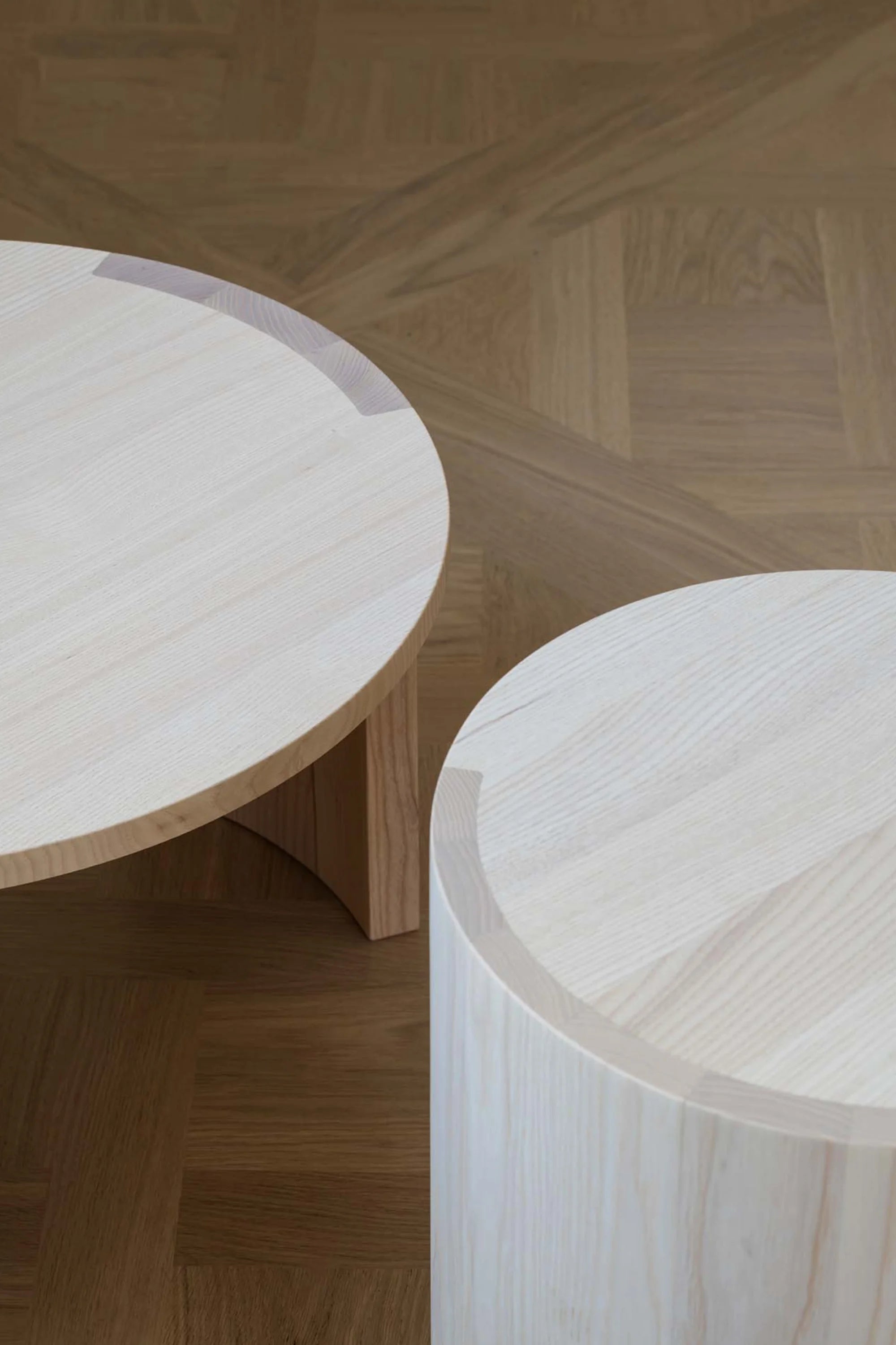 Two wooden airisto side tables on a wooden floor with a herringbone pattern.
