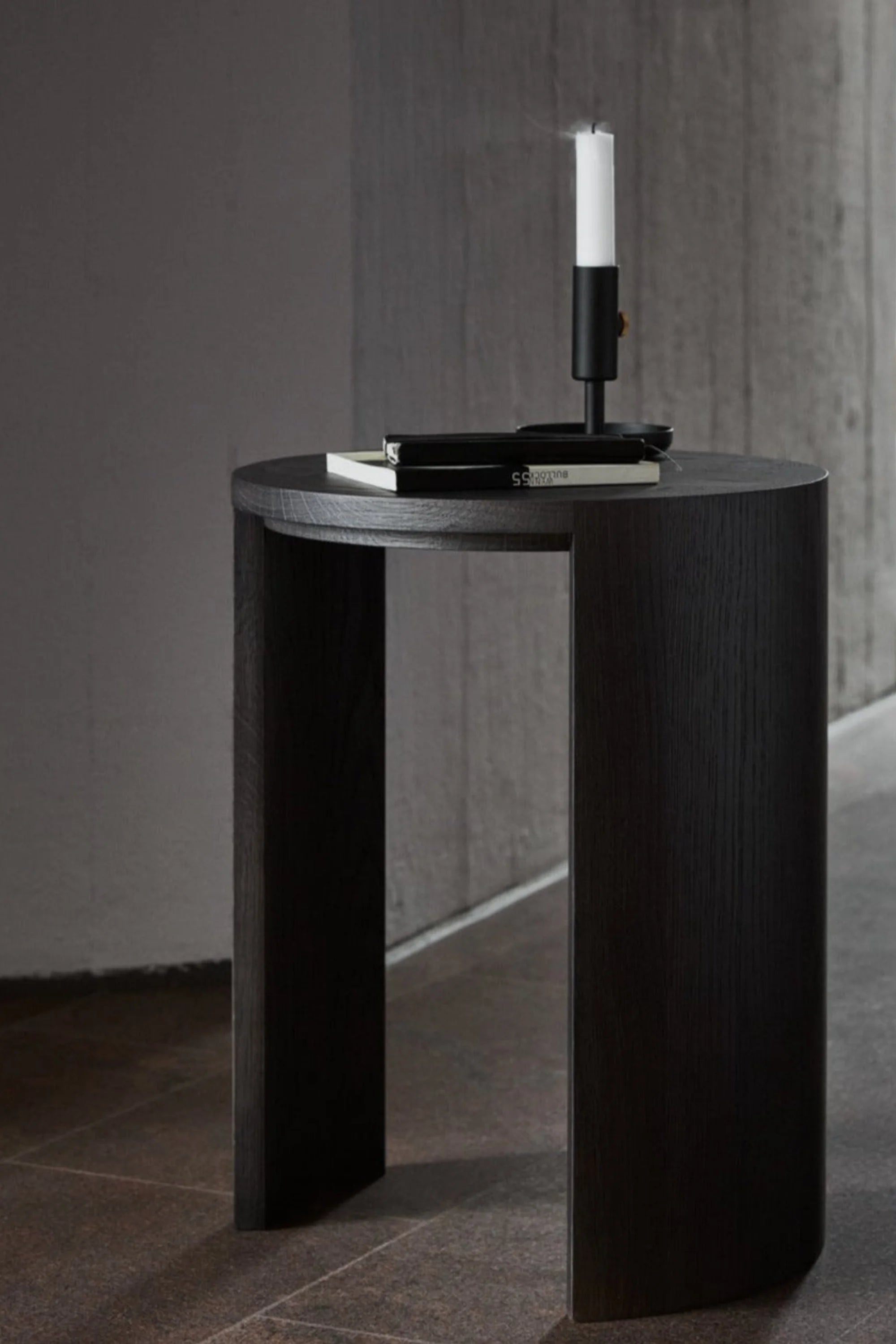 Black cylindrical side table with a candle and phone on a gray background