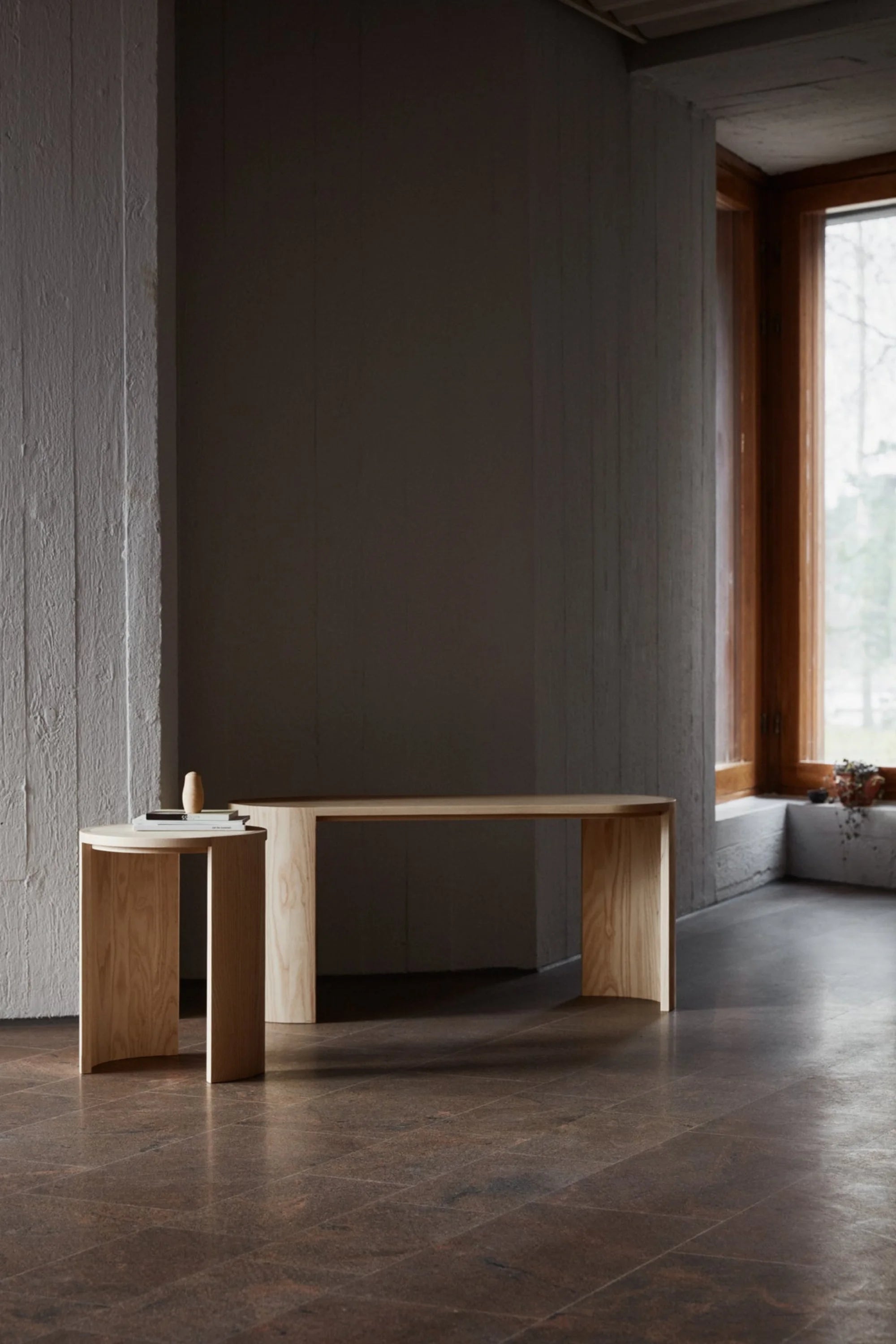 Minimalist wooden bench against a gray wall in a room with large windows.