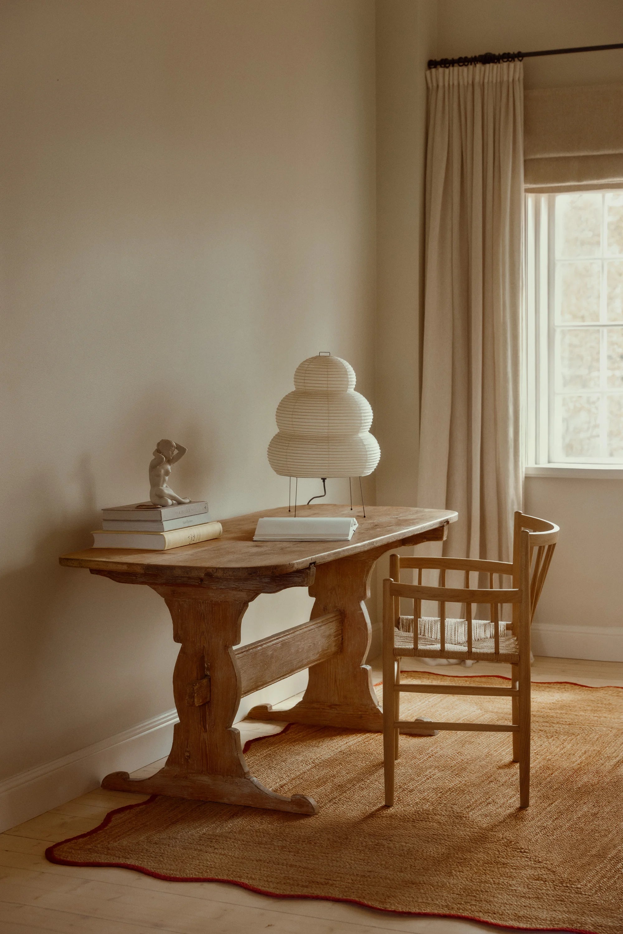 Wooden table with a lamp and books in a room with a window and curtains.