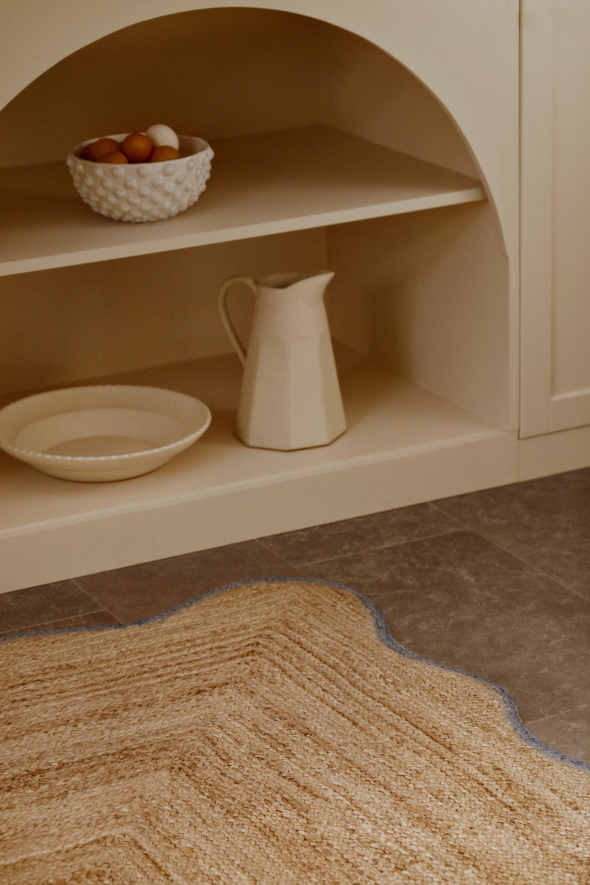 Ceramic pitcher and bowl on a shelf with a textured rug in the foreground