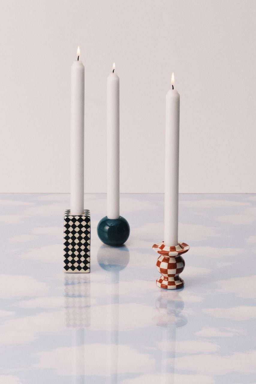 Three candles in decorative holders on a reflective surface with a light gray background