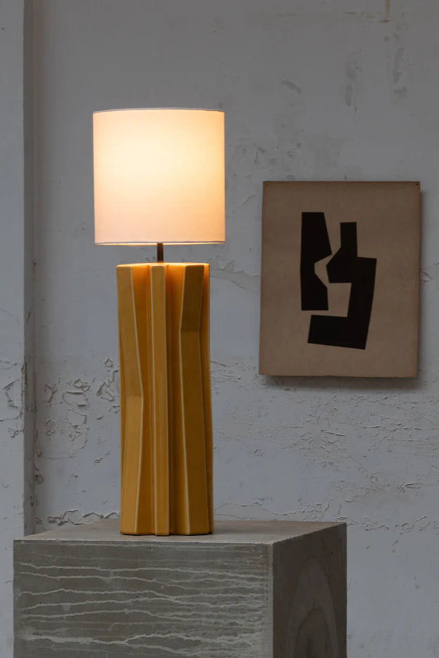 Yellow table lamp on a gray pedestal with abstract wall art in the background