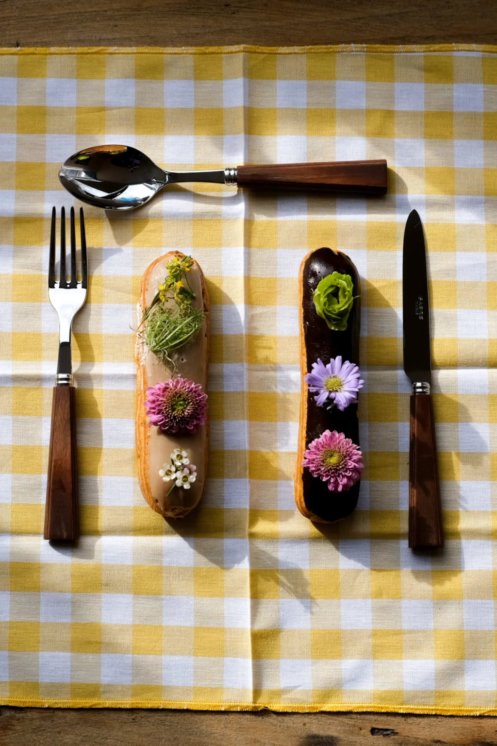 Sabre Paris Nature 4-Piece Cutlery Flatware Set, featuring polished stainless steel utensils with elegant rich brown wooden handles, arranged on a yellow and white checkered tablecloth. This stylish cutlery set is perfect for enhancing everyday dining and special occasions for those who appreciate natural appeal.