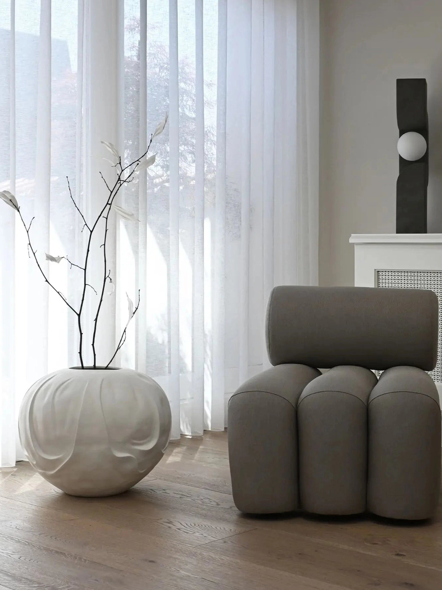 101 CPH Foku Lounge Chair in a modern light grey fabric, featuring a cylindrical backrest and three bulbous upholstered legs, styled on light wooden floor. A premium accent for contemporary interiors.