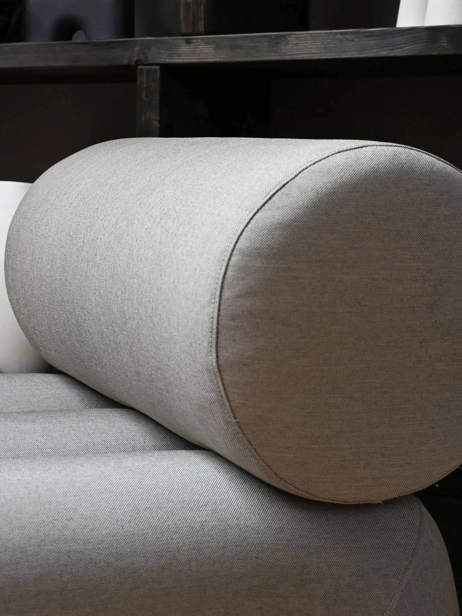 101 CPH Foku Lounge Chair, showcasing its light grey fabric upholstery with visible woven texture, cylindrical bolster cushion, and tailored piped seams. This premium design offers luxurious comfort.