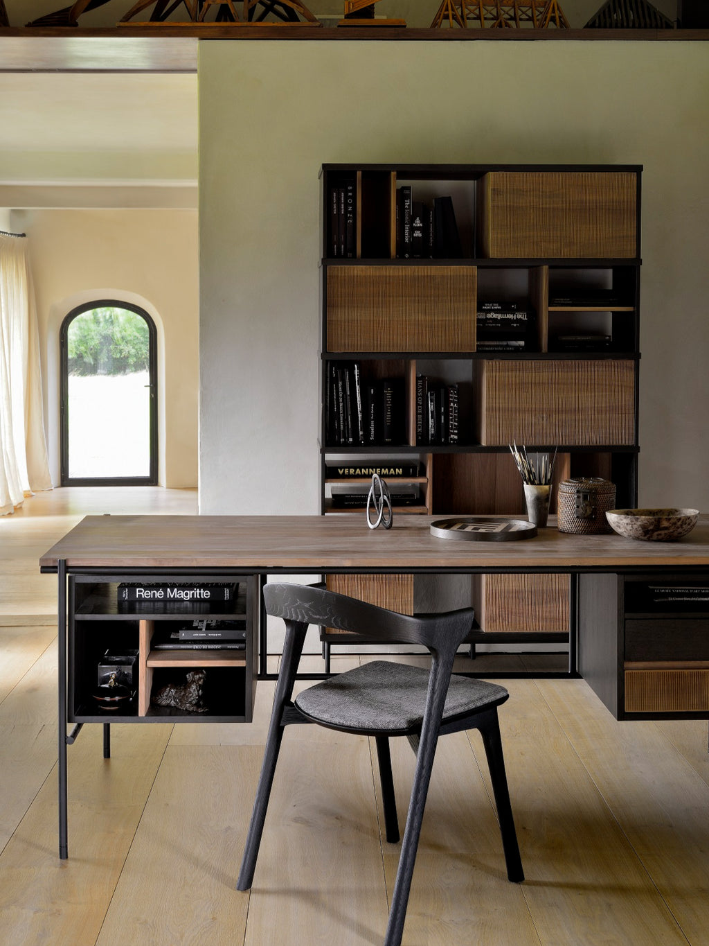 Ethnicraft Oscar Desk, a modern wooden desk with dark brown finish, integrated shelving, and a matching chair, set in a stylish home office with a large window.