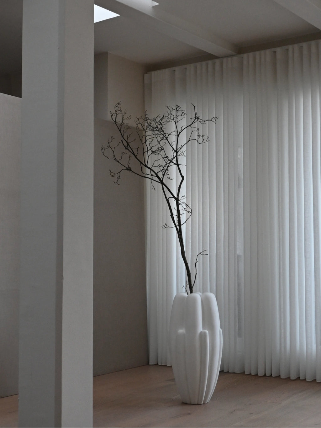 101 CPH Bloom Slim Vase: A tall, white, organically textured, and sculptural ceramic vase with a matte finish, housing dry branches in a modern room. An authentic, luxury decorative art piece for contemporary interiors.