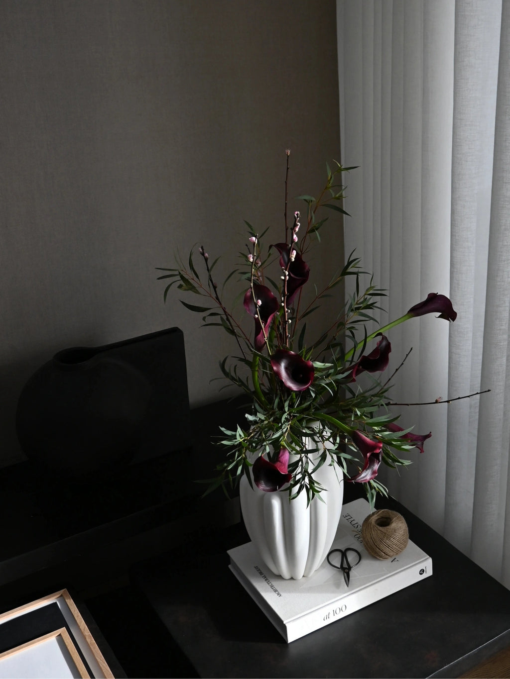 101 CPH Bloom Slim Vase in off-white textured ceramic, fluted design, holding striking deep purple calla lilies & greenery on stacked white books. A luxurious home decor accent.
