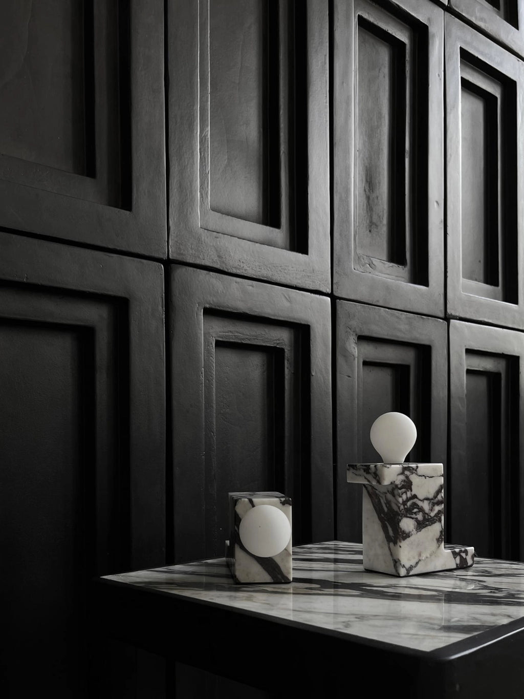 101 CPH Brick Lamp: Two luxury black-and-white marble lamps with white spherical bulbs, one cube-shaped, one L-shaped, displayed on a glossy marble surface against a black geometric wall for sophisticated ambient lighting.