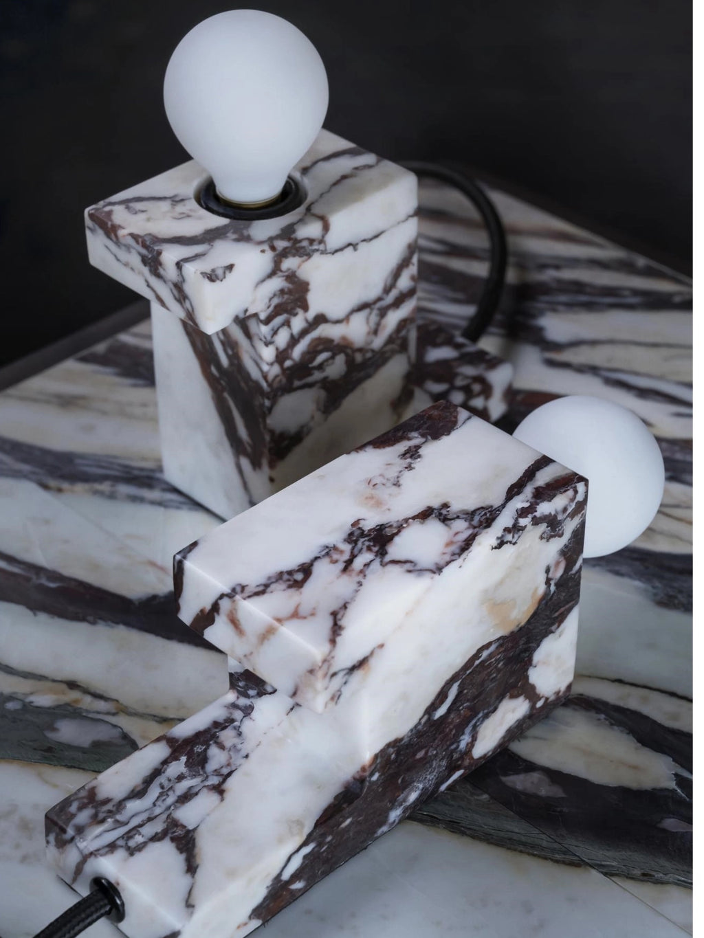 101 CPH Brick Lamp: Two premium rectangular blocks of white marble with dramatic brown and black veining, displayed on a matching marble surface. Each modular lamp features a frosted white bulb and a sleek black cord. Ideal for modern interior design.