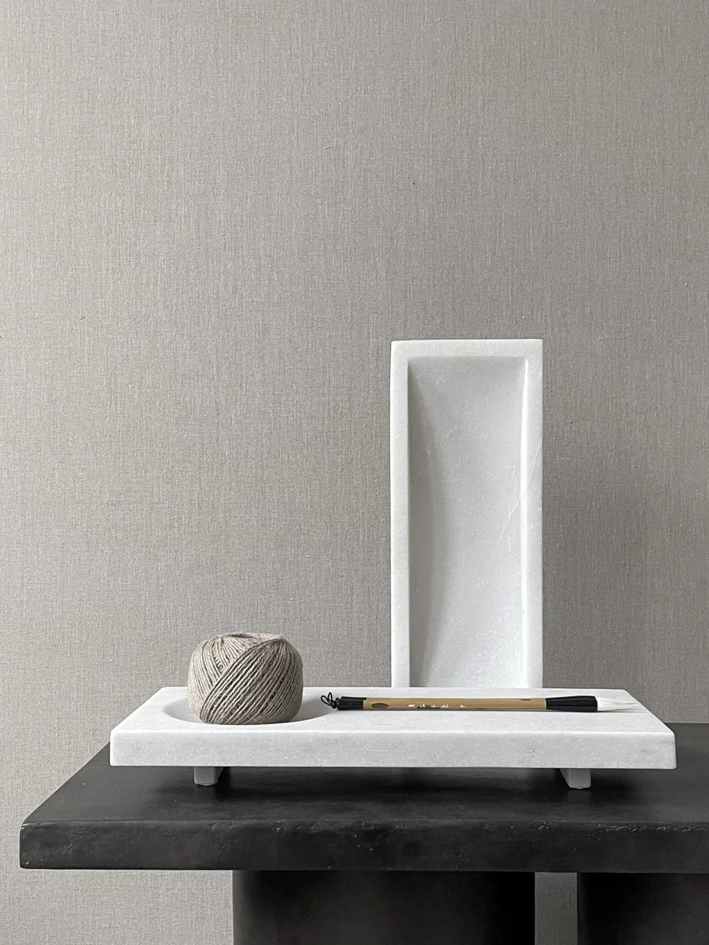 101 CPH Formalism Tray: White honed marble with subtle gray veining, displayed on a black surface. This premium rectangular decorative tray features elevated feet, with a standing matching accessory behind it, and a spool of twine and calligraphy brush placed on it. Ideal for sophisticated home decor.
