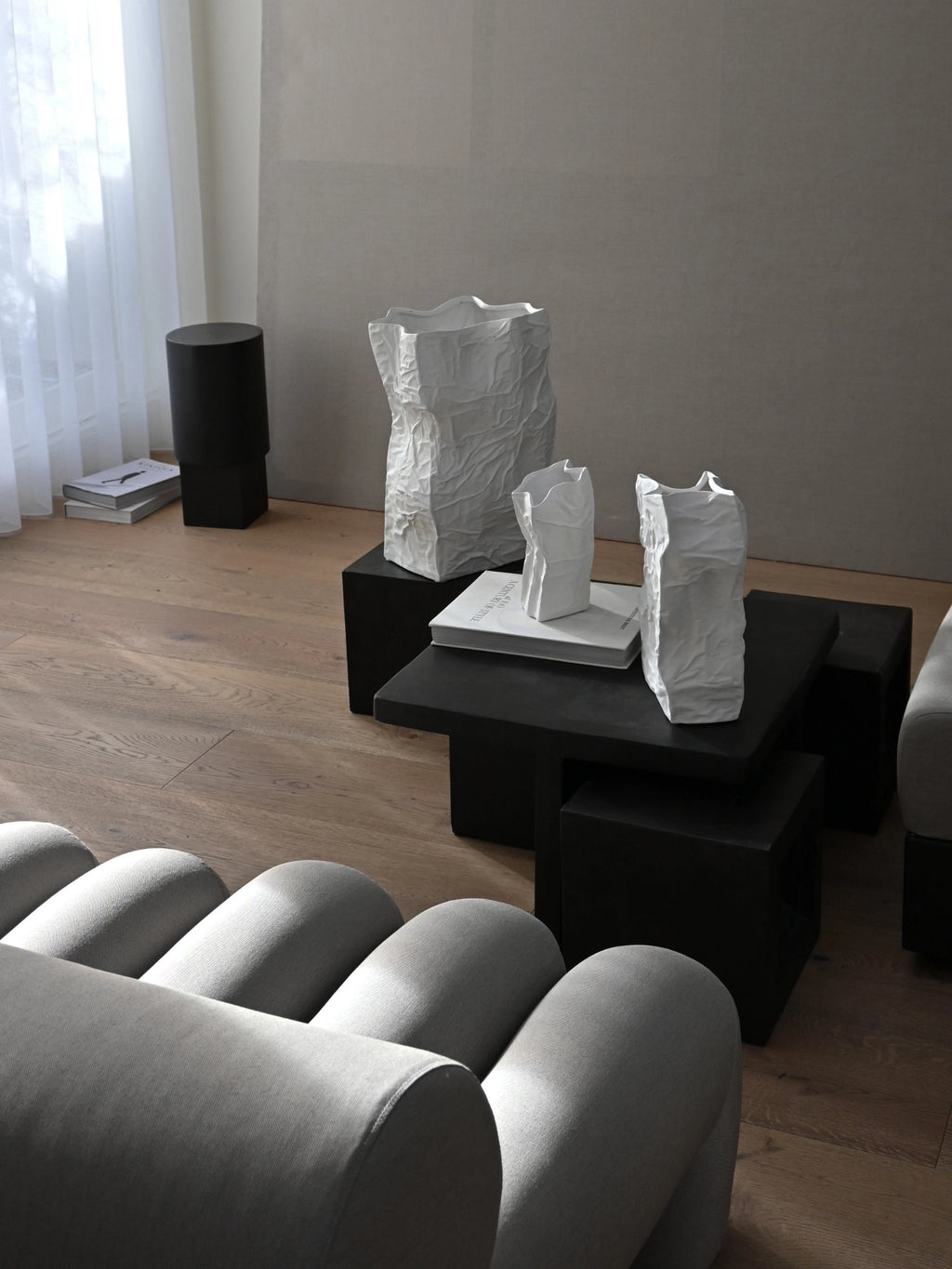 101 CPH Kami Vase, a set of three white ceramic vases in a crinkled, paper bag-like design, displayed on a black coffee table in a modern living space. Perfect for showcasing unique botanicals.