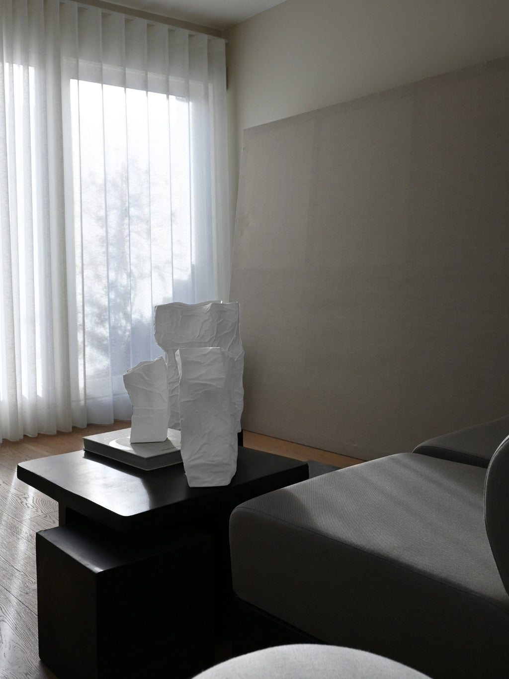 101 CPH Kami Vase collection: Three unique, handcrafted white ceramic vases with crumpled, paper-like textures, artfully displayed on a black coffee table in a modern living room setting. Ideal for contemporary decor.