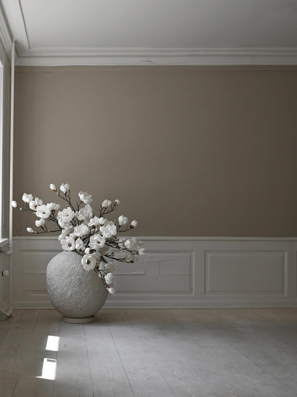 101 CPH Sunao Planter: A large, round, light grey textured ceramic planter, filled with white magnolia blooms, displayed in a minimalist room with natural light. Ideal for sophisticated home decor.
