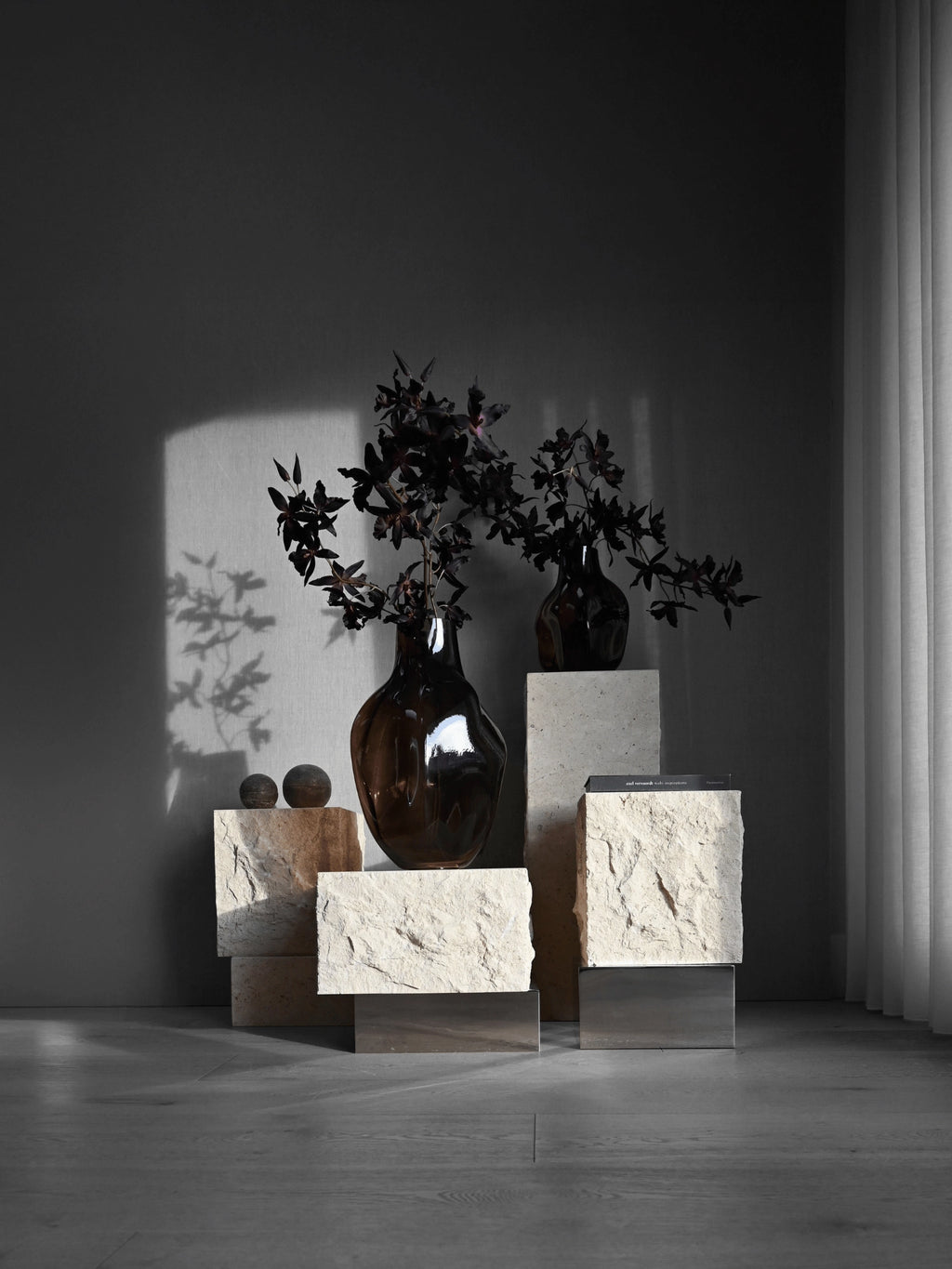 101 CPH Temple Coffee Table Set, featuring rough-hewn cream stone blocks and polished metal bases in a dynamic, staggered display. Two dark amber glass vases with deep red foliage and small earthy spheres are arranged on top, creating a luxurious, artful centerpiece for modern living.