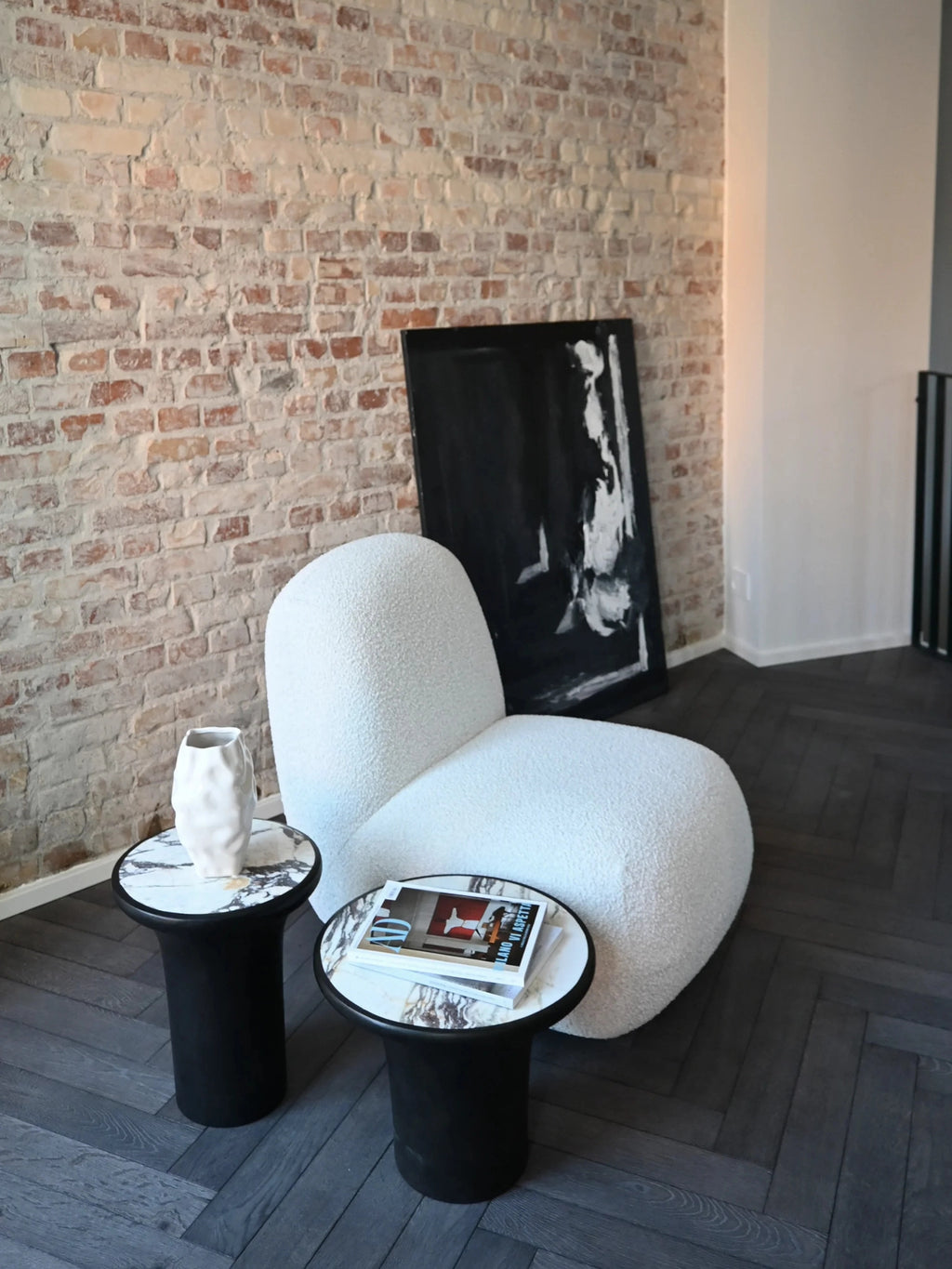 101 CPH Trumpet Side Table features a striking black cylindrical base with a luxurious white and gray marble top, styled next to a bouclé chair. A premium accent for any modern living space.