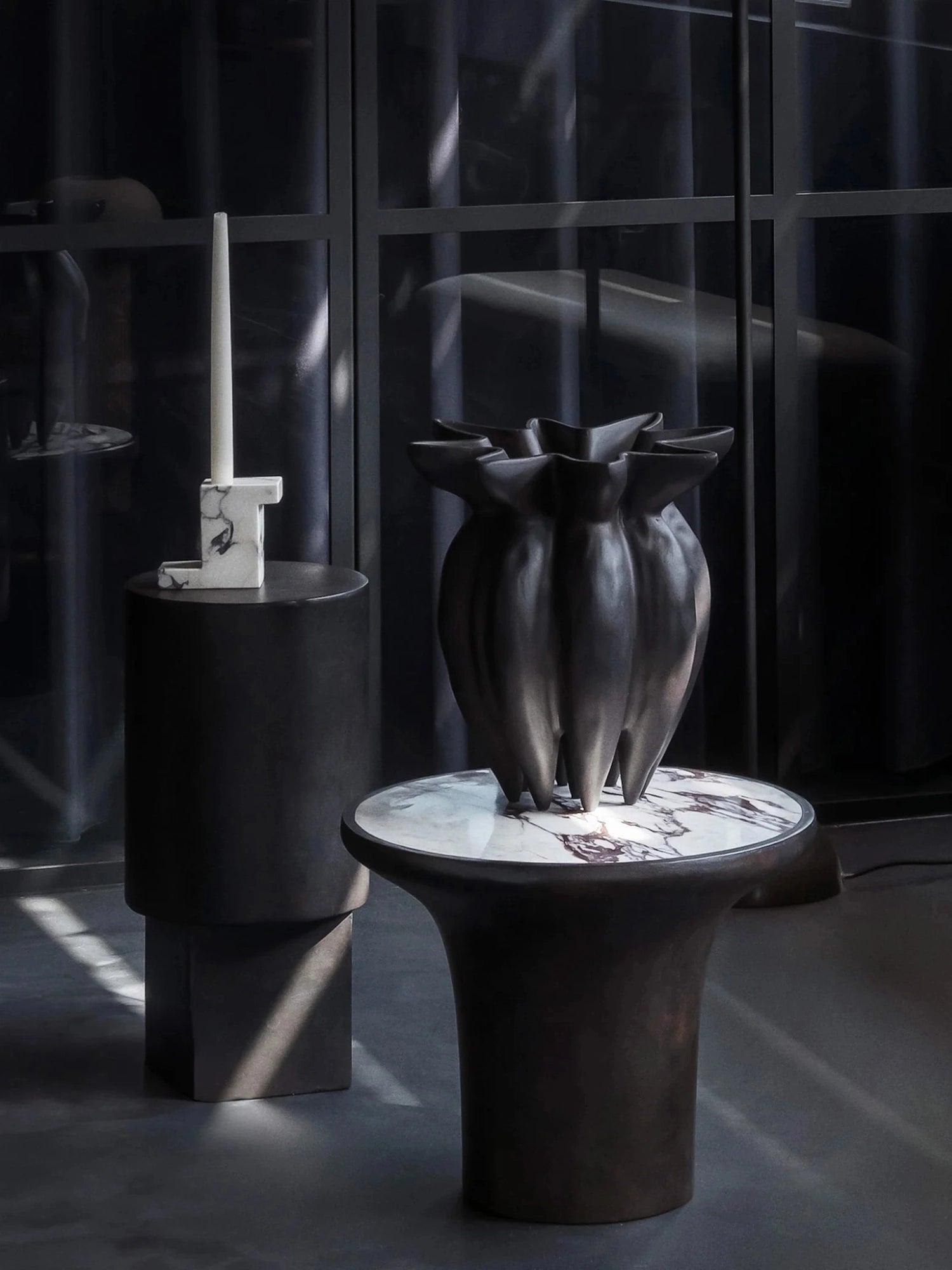 101 CPH Trumpet Side Table, a dark bronze sculptural piece with a white and brown veined marble top, displayed in a dark, minimalist interior. A luxury accent for modern living spaces.