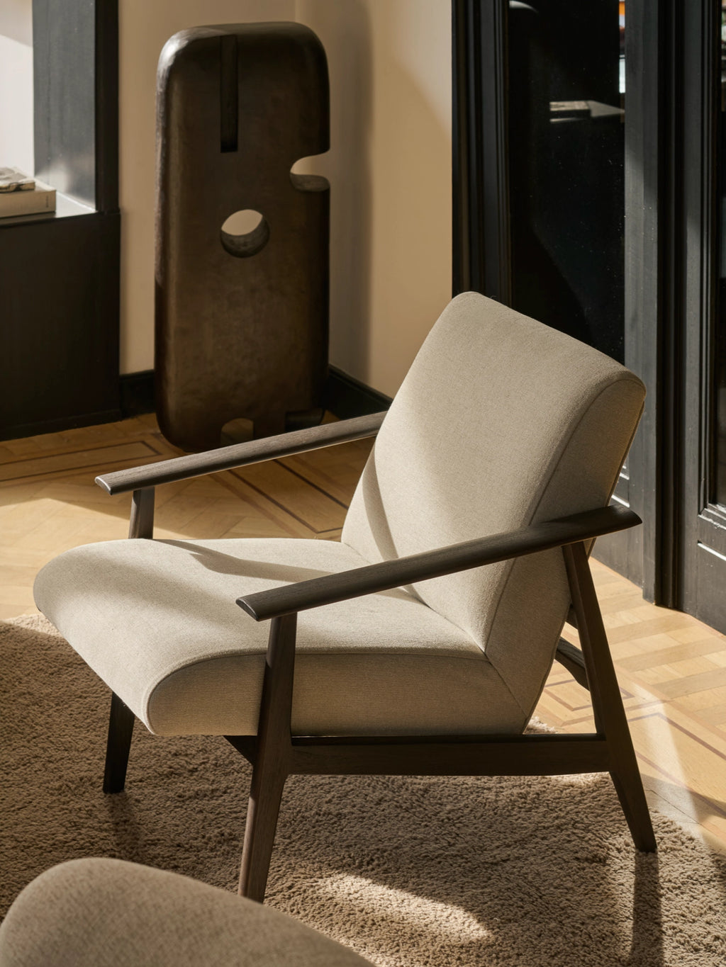 Ethnicraft Aspekt Lounge Chair, a sophisticated mid-century modern accent chair featuring a dark stained solid oak wood frame with elegantly curved armrests and tapered legs. It is upholstered in a light beige textured fabric, offering a minimalist yet inviting design, perfect as a stylish lounge chair for contemporary living rooms or cozy reading nooks.