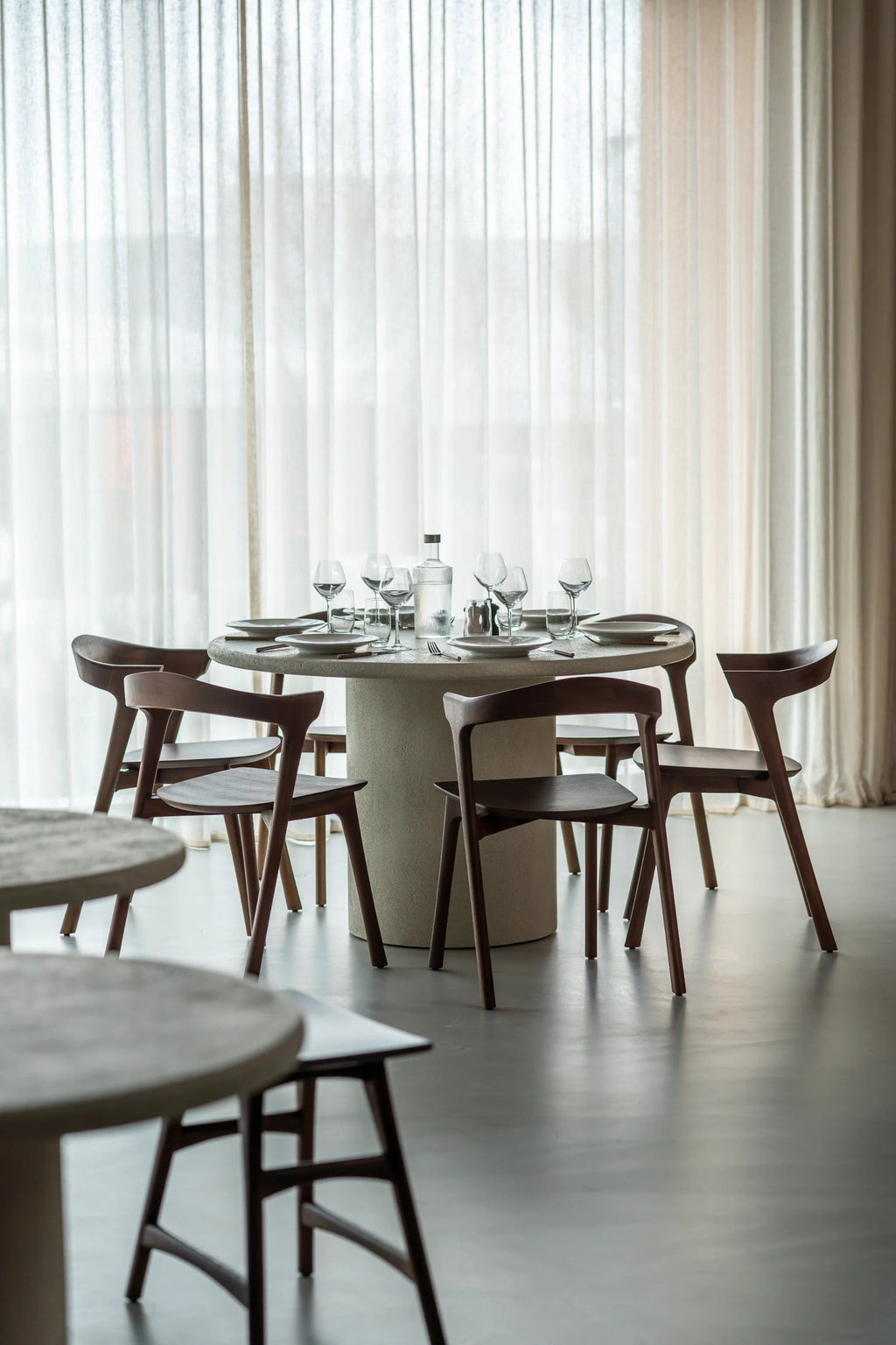 Ethnicraft Elements Dining Table, a modern minimalist round dining table featuring a light grey textured concrete tabletop and a sturdy cylindrical pedestal base, embodying an organic modern design.