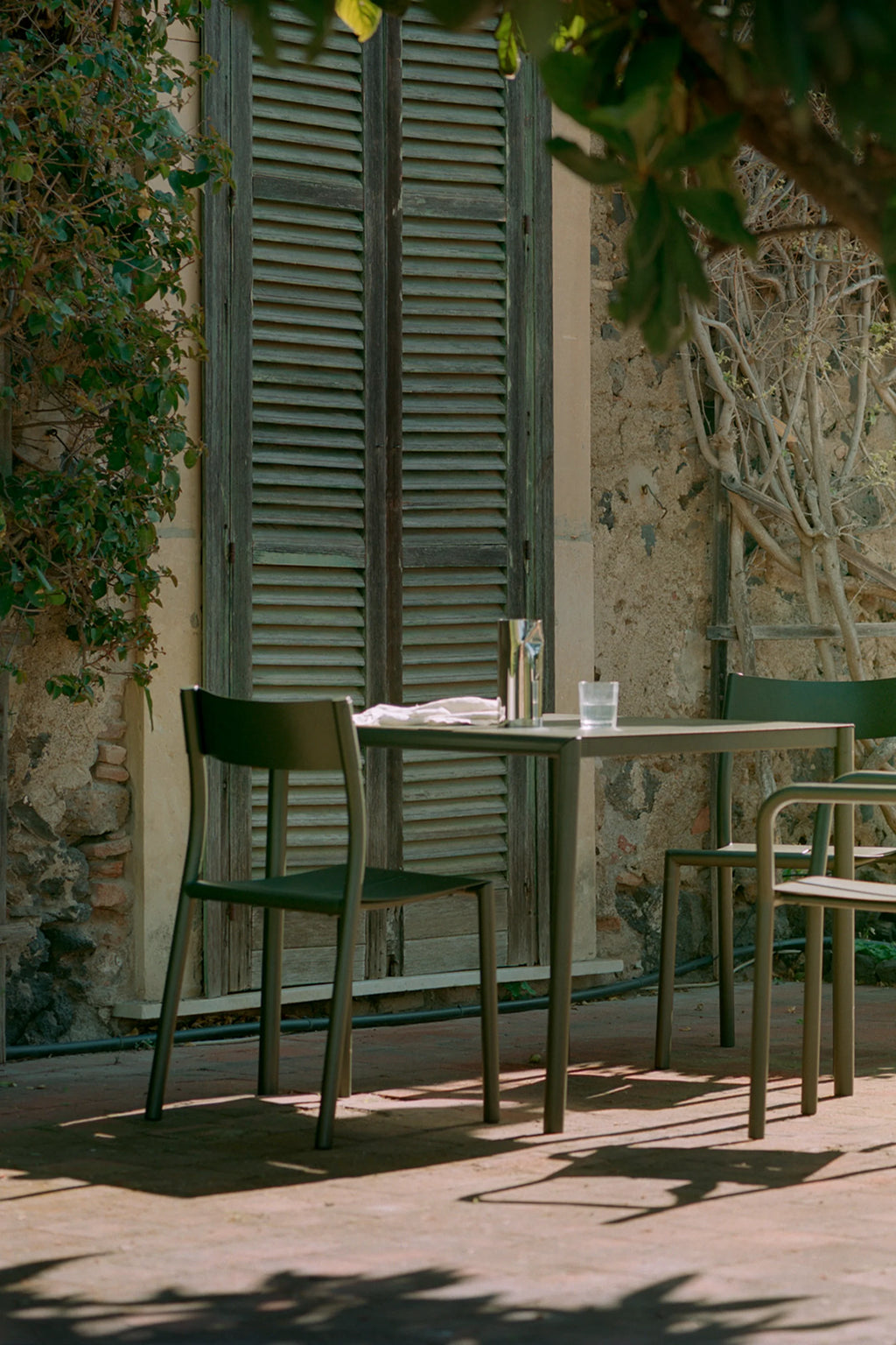 New Works Outdoor May Furniture Set for 2 Persons, a modern minimalist outdoor dining set crafted from durable powder-coated metal in a deep olive green finish. The set includes a sleek rectangular outdoor table and two matching contemporary chairs with clean lines and a smooth, matte texture. Ideal as a stylish 2-person patio set, Scandinavian balcony furniture, or a compact garden bistro set for contemporary outdoor living.