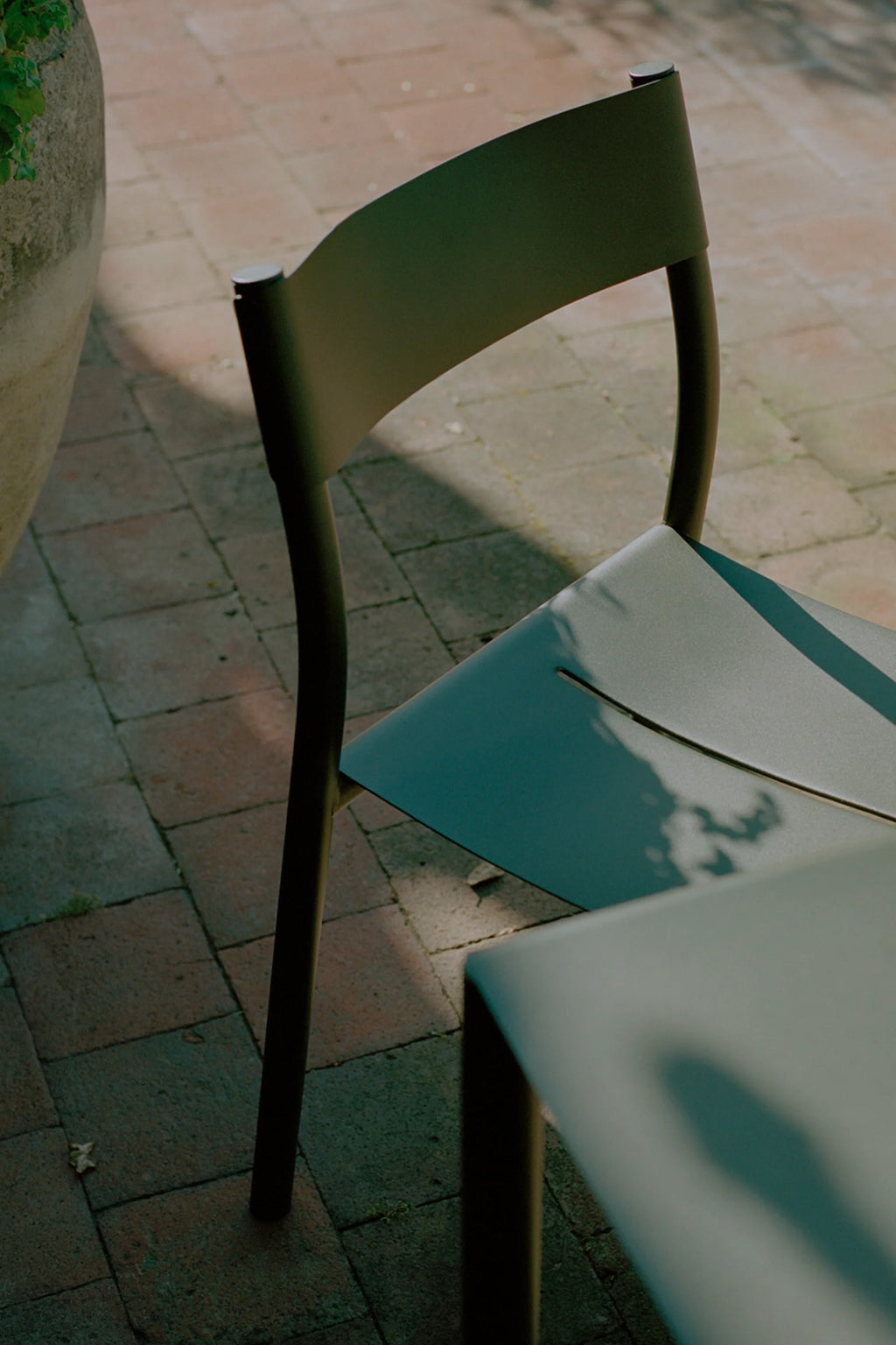 New Works Outdoor May Furniture Set for 4 Persons, featuring a sleek, modern minimalist chair and partial table in a matte dark olive green powder-coated metal finish. The chair showcases a sculptural, curved backrest and angled seat, reflecting contemporary Scandinavian design. This durable outdoor dining set is perfect for stylish patio dining, garden entertaining, or a chic balcony setup.