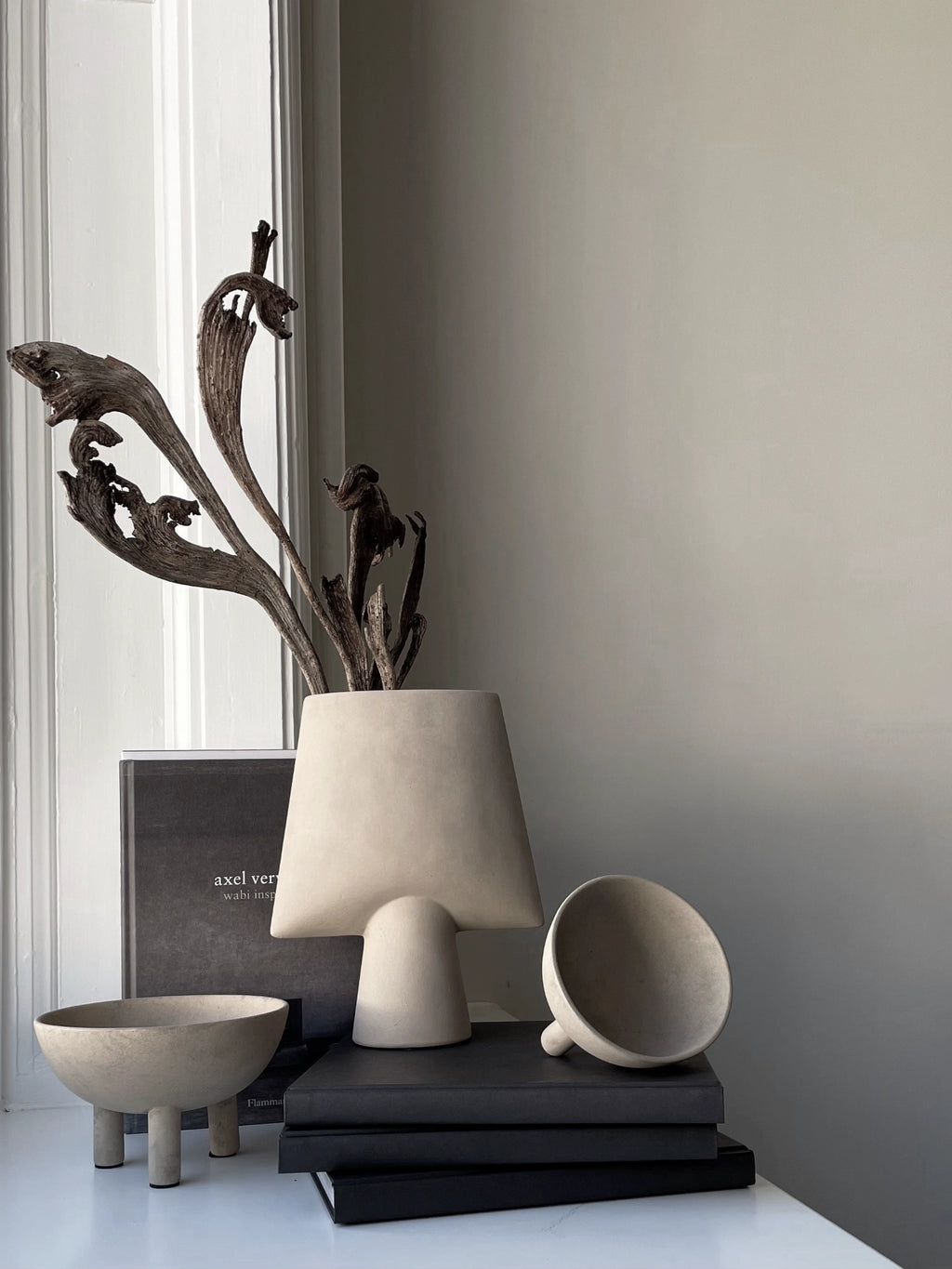 101 CPH Duck Bowl, an authentic beige concrete bowl with three short, round legs, styled on a white surface next to books. A premium sculptural accent for modern interiors.