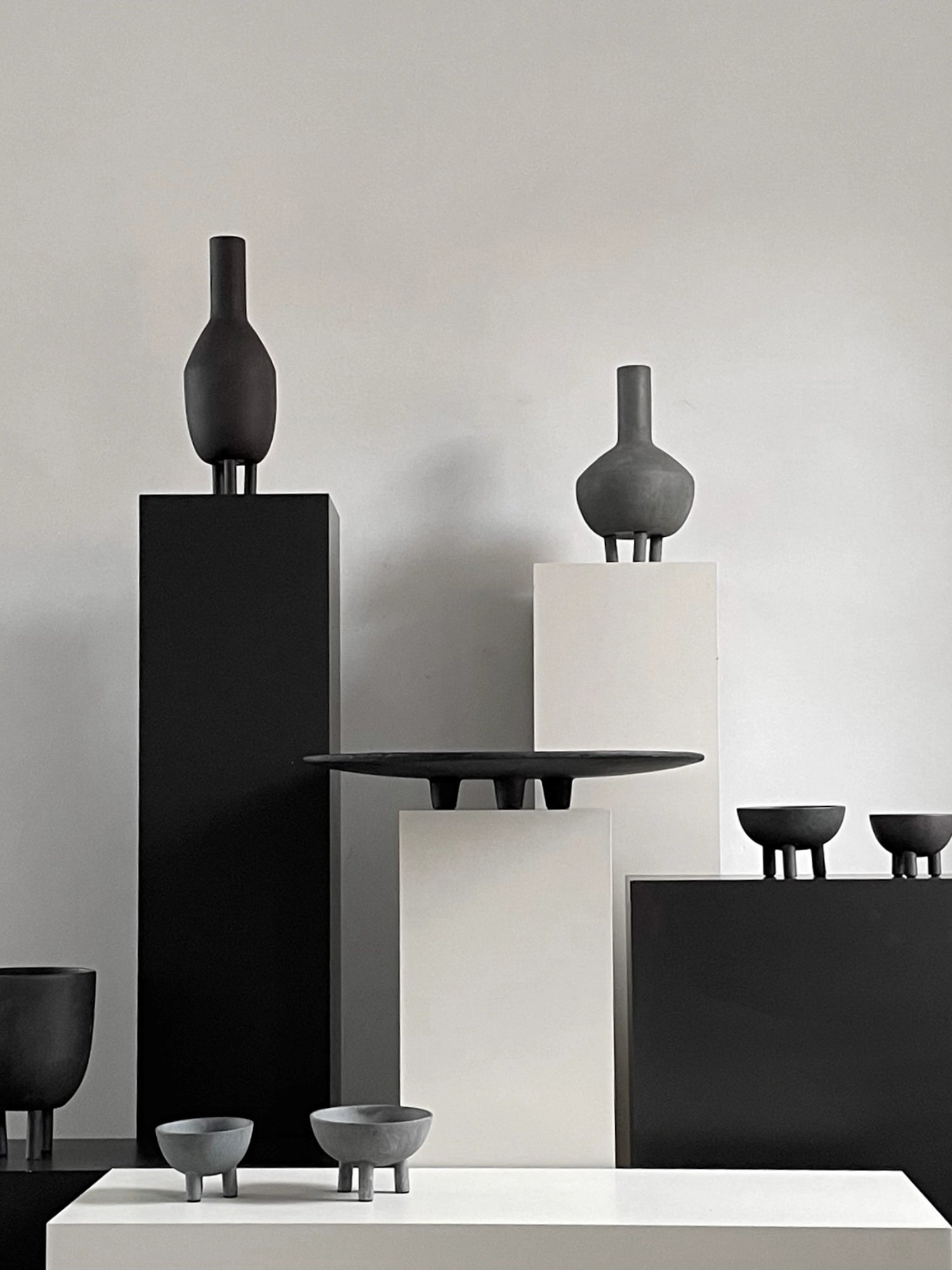 101 CPH's Duck Bowl, showcased in a lifestyle setting, are charcoal grey ceramic bowls with three distinct stubby legs. Several premium matte dark grey home decor elements are artfully arranged. Ideal for modern interior styling.