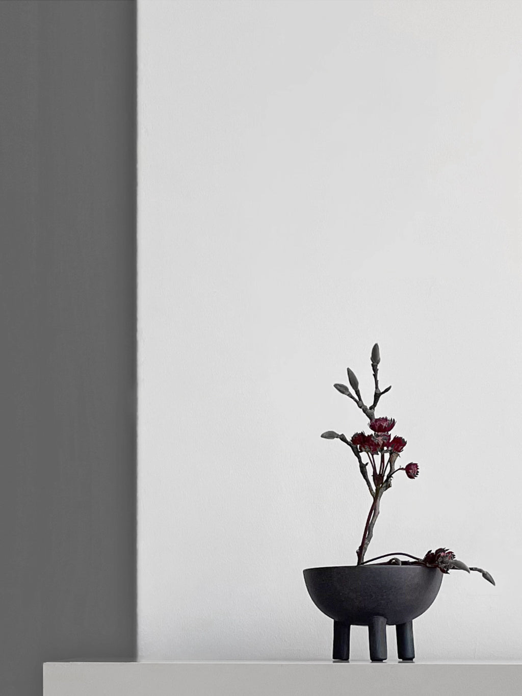 101 CPH Duck Bowl, an authentic dark charcoal grey stoneware bowl with three cylindrical legs, displaying dried red flowers. A premium decorative piece for modern interiors.