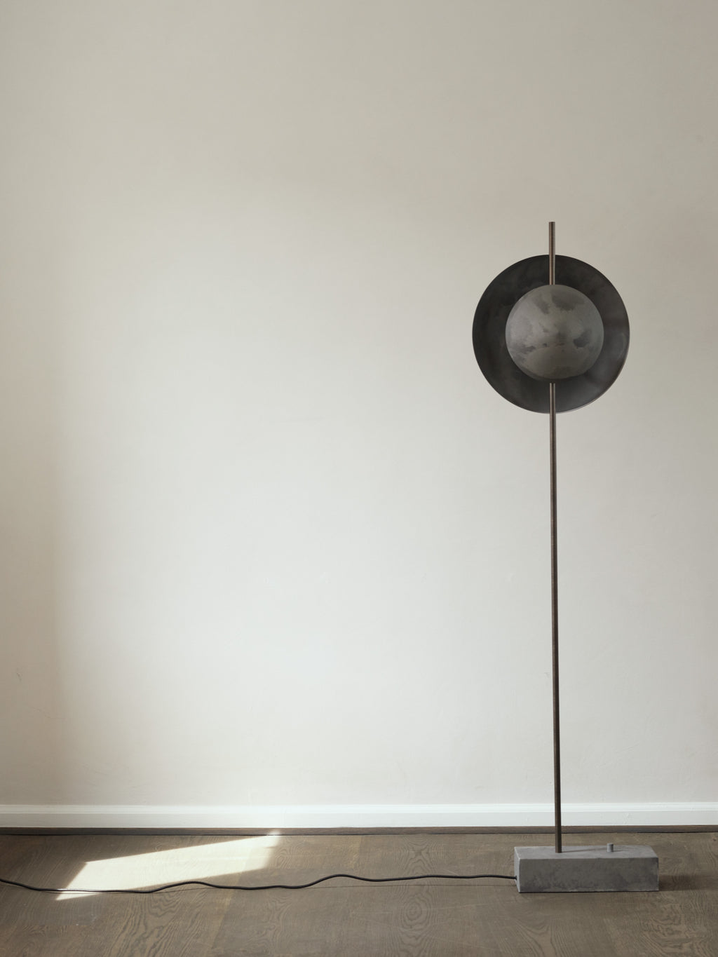 101 CPH Dawn Floor Lamp in a flat lay, featuring a dark grey round metal shade and a smaller textured gray spherical bulb, on a slim bronzed metal pole with a rectangular raw concrete base. A premium, modern lighting solution.