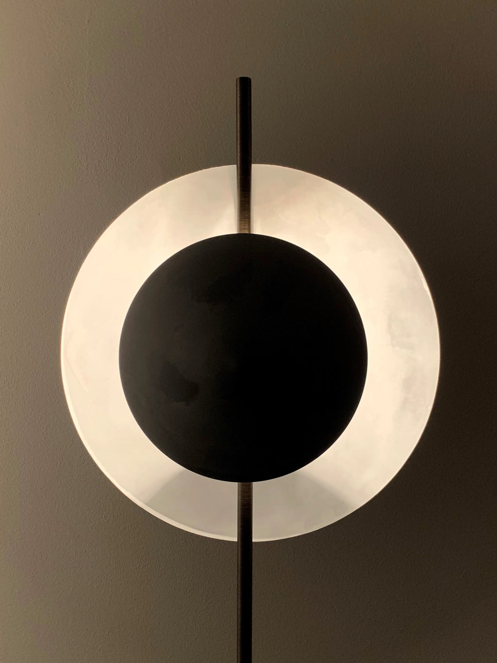 101 CPH Dusk Table Lamp features a cream alabaster-like backlit circular diffuser with a matte black metal disc overlay, centered on a dark vertical rod. A true luxury design piece for contemporary interiors.