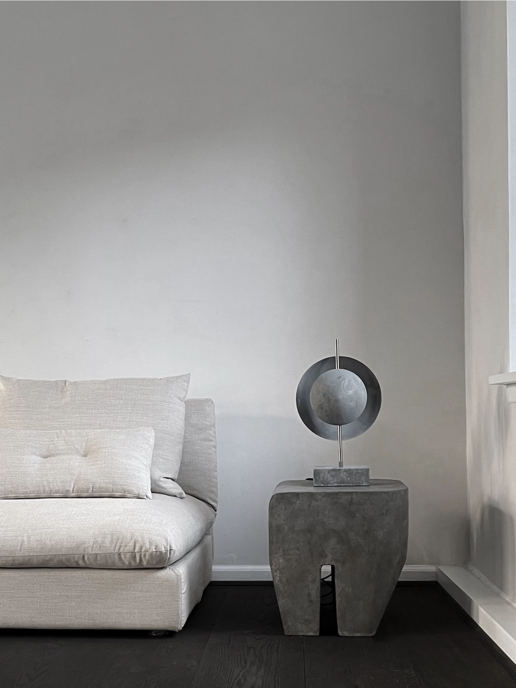 101 CPH Dusk Table Lamp, a modern sculptural piece with a dark grey concrete base and a circular metallic shade, featuring a unique textured finish in a contemporary living room setting. Ideal for sophisticated interior design.