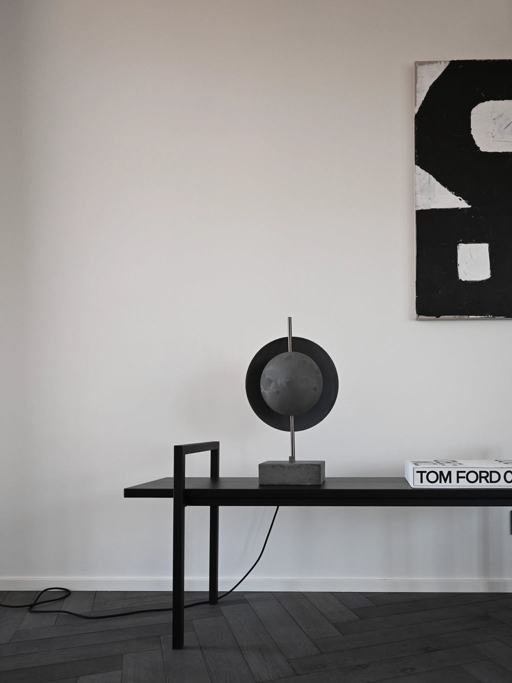 101 CPH Dusk Table Lamp features a dark gray spherical diffuser encased by a black metal ring, set on a industrial concrete base and thin metal rod. Ideal for premium modern interiors.