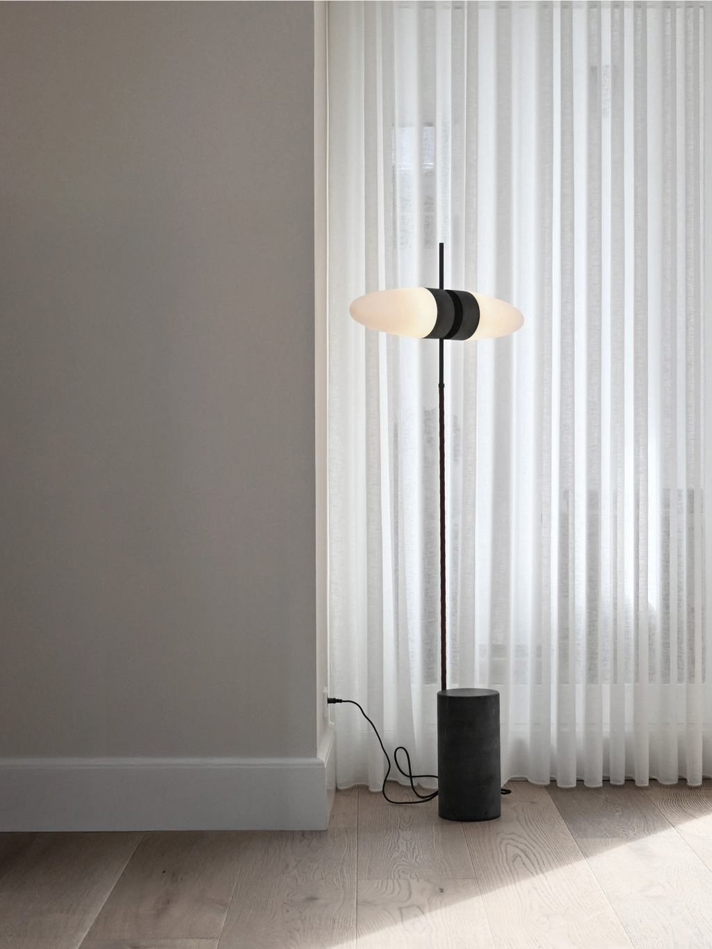 101 CPH Bull Floor Lamp in a modern living space. This minimalist black metal lamp features a cylindrical stone-like base and two oblong, frosted white glass diffusers for premium ambient lighting. Ideal for enhancing contemporary interiors.