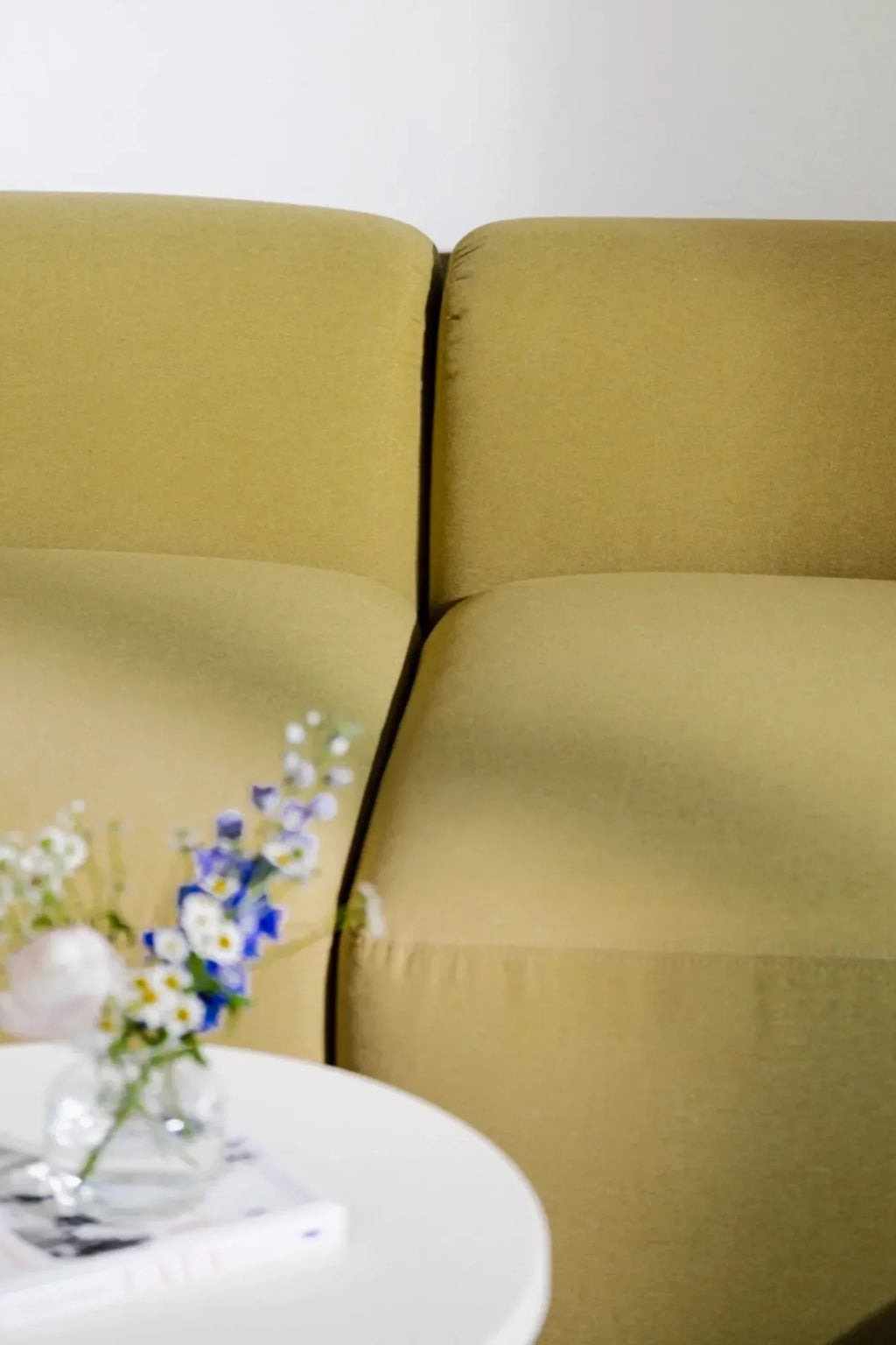 noo.ma Flom 2-Seater Sofa, a contemporary minimalist sofa upholstered in a rich, textured chartreuse fabric, featuring plush, deep cushions and a clean, inviting silhouette. This modern design with soft, rounded edges is ideal for creating a cozy yet stylish focal point in small living rooms or studio apartments.