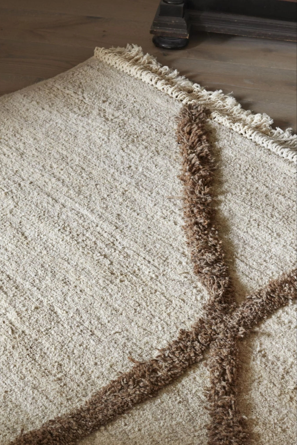 Sera Helsinki Vuoristo Rug, a plush hand-knotted wool area rug featuring a natural undyed cream background with a bold, shaggy brown geometric pattern and a distinctive fringed edge. This textured rug offers a cozy, organic modern aesthetic perfect for Scandinavian living rooms, boho bedrooms, or rustic-chic interiors.